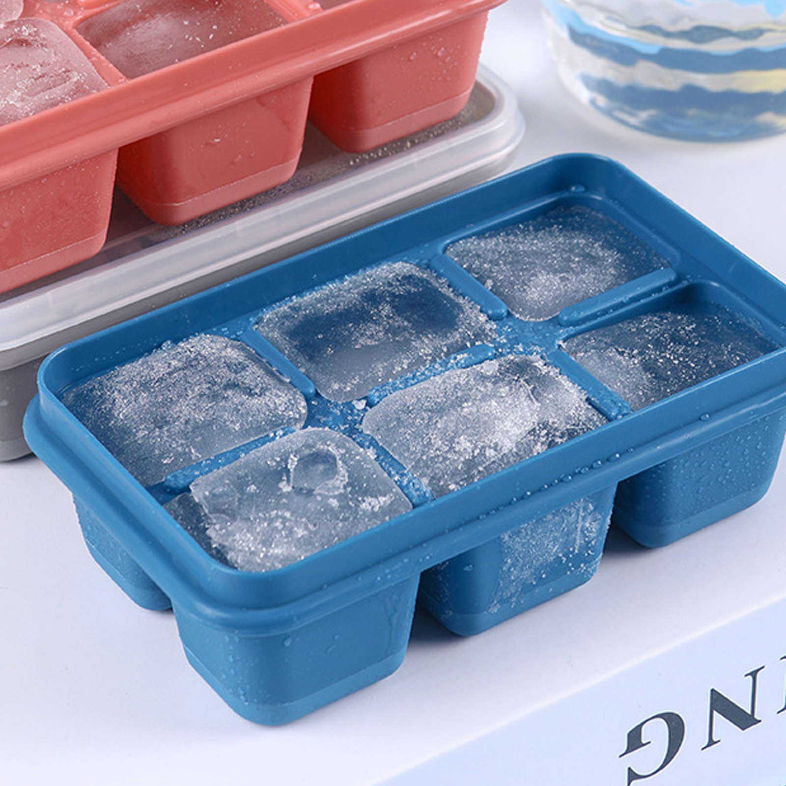 Blaue Eiswürfelform mit Eiswürfeln gefüllt, neben einer rosa Form.
