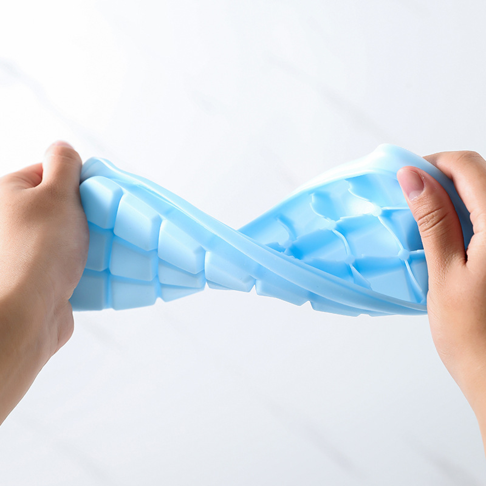 Hände biegen eine blaue Eiswürfelform mit vielen Würfeln.