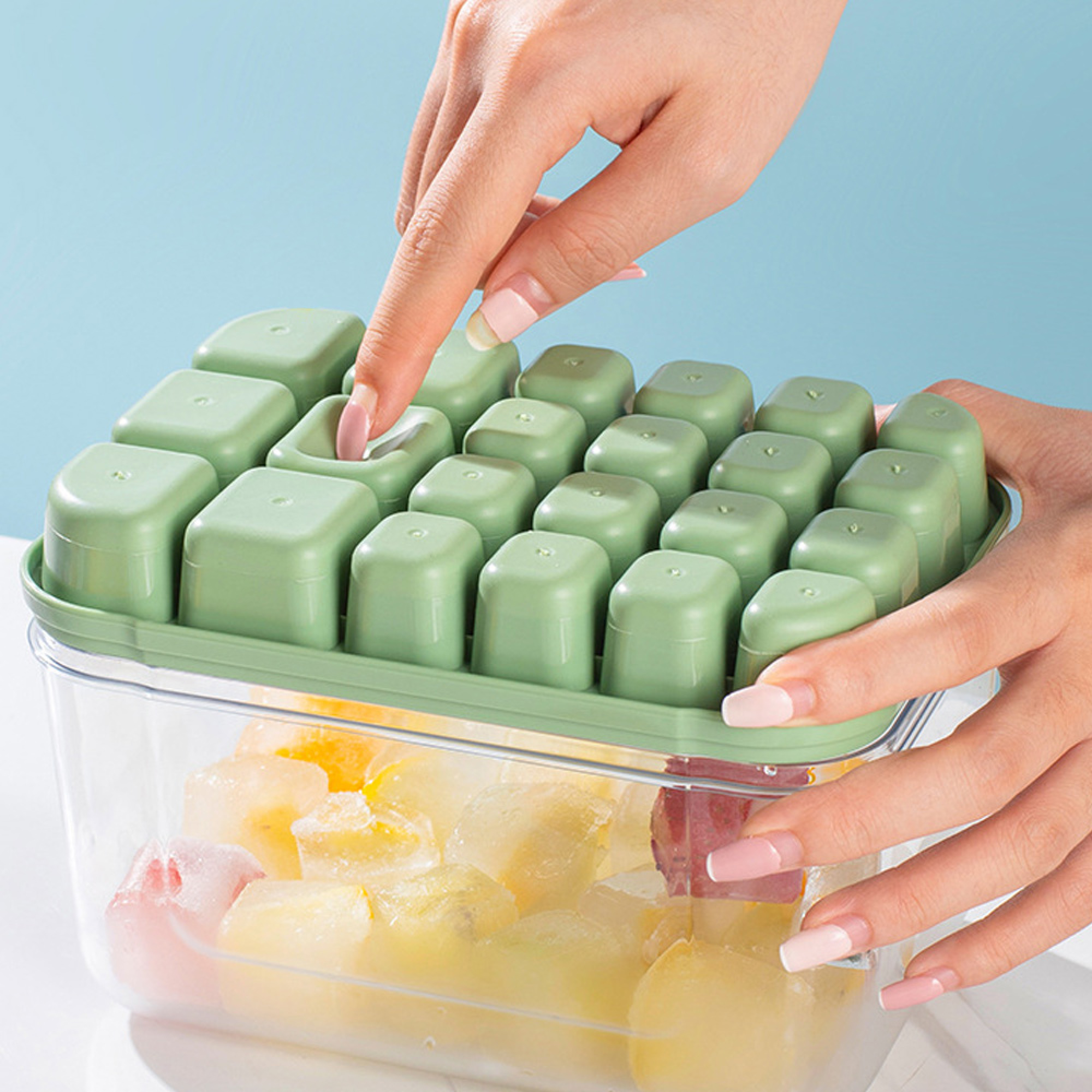 Eine Hand entnimmt einem grünen Eiswürfelbereiter mit Deckel einen Eiswürfel.