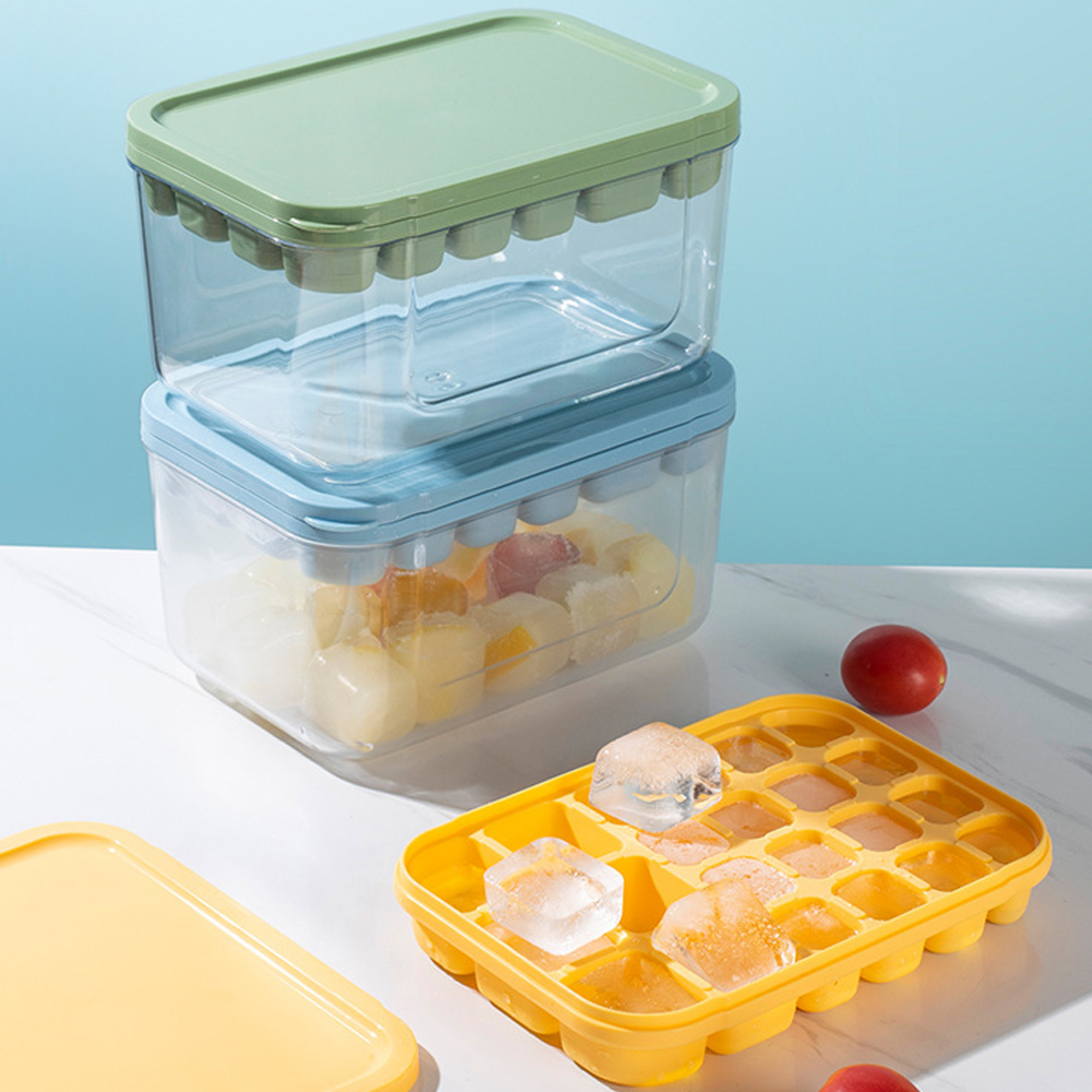 Zwei Eiswürfelbehälter, einer mit blauem und einer mit grünem Deckel. Ein Eiswürfelbehälter mit Eiswürfeln.