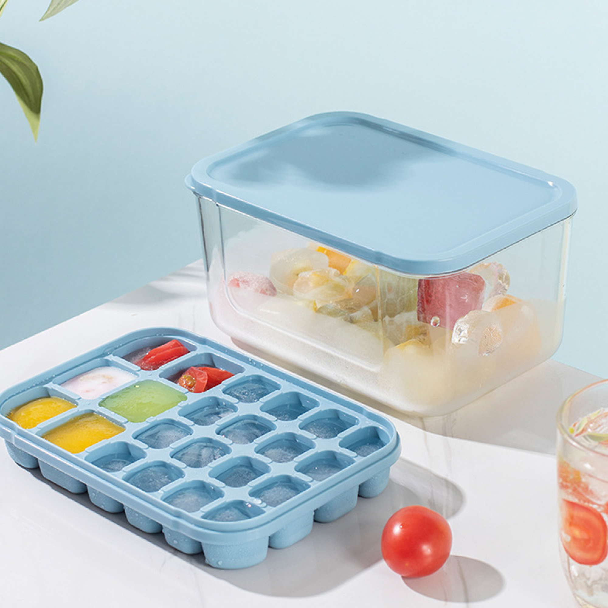 Blaue Eiswürfelform mit gefrorenen Früchten und Eiswürfeln, daneben eine Aufbewahrungsbox.