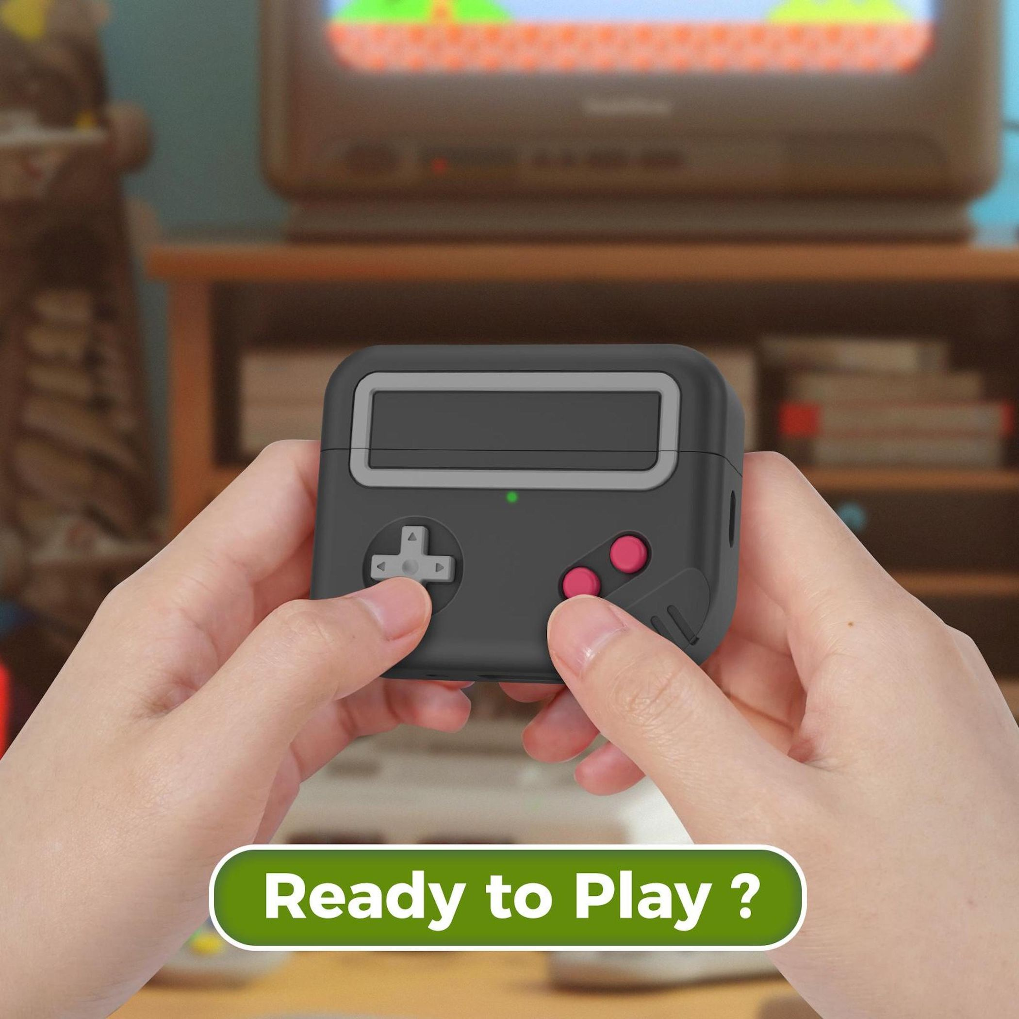 Hände halten eine schwarze Retro-Spielkonsole mit pinken Knöpfen. Im Hintergrund ein Fernseher.