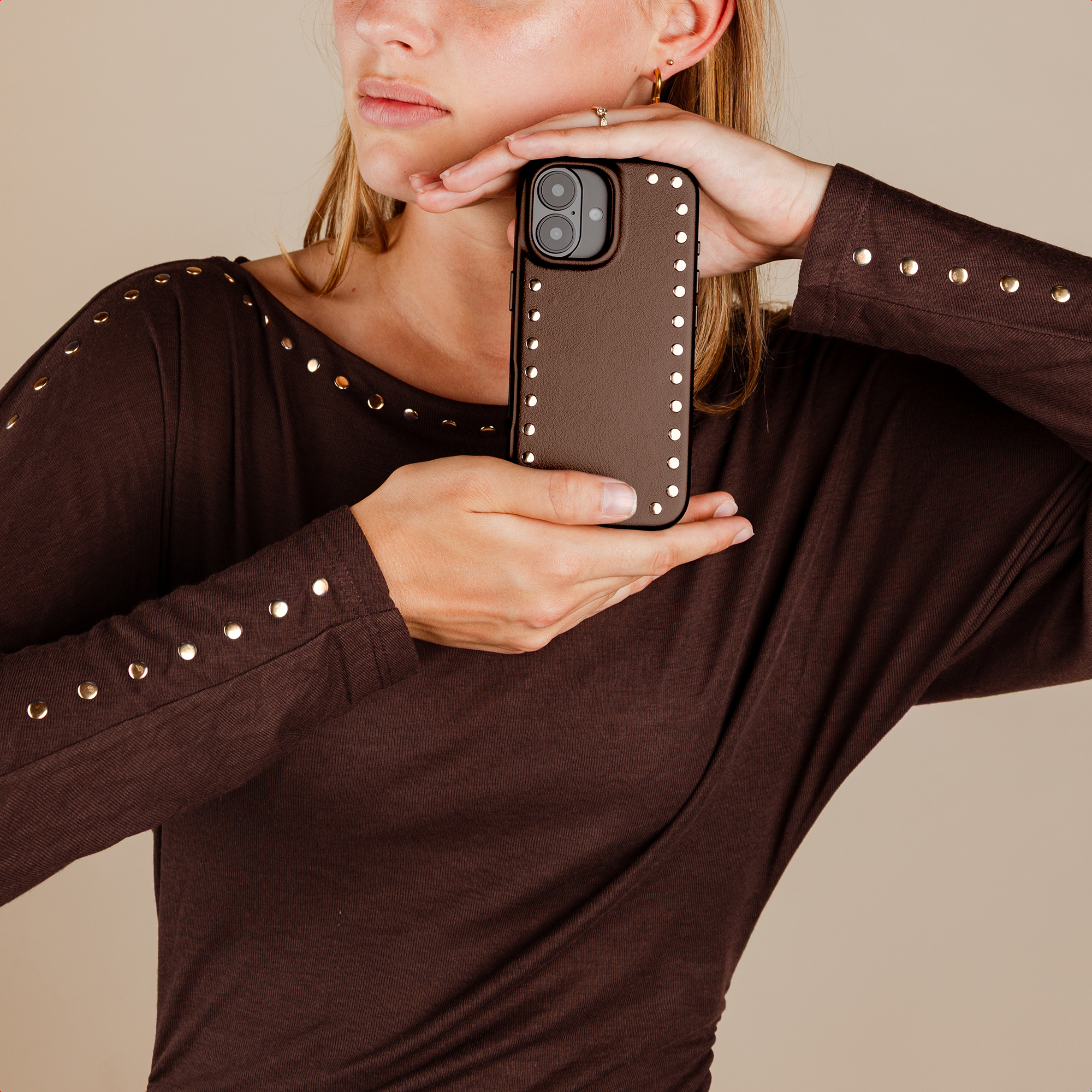 A woman holds a brown phone case with studs.
