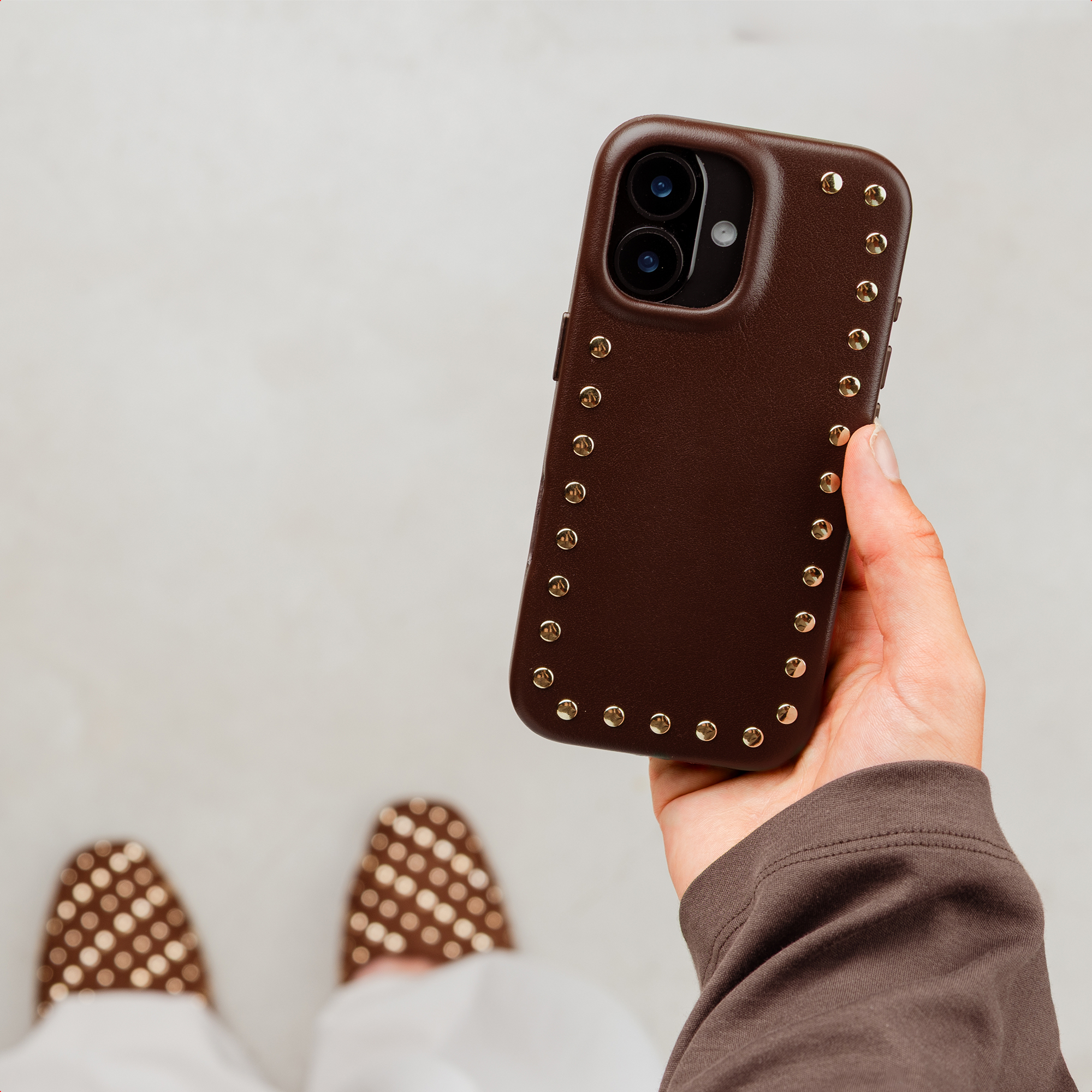 Brown studded phone case on a phone held in a hand.