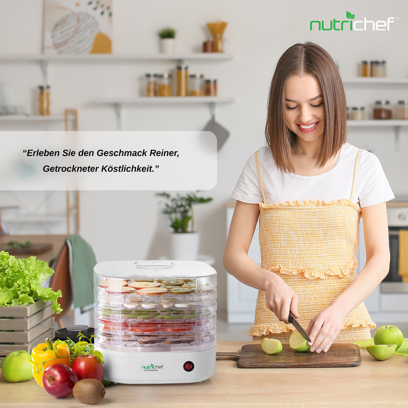 Frau schneidet Äpfel neben einem Dörrgerät mit Obst in einem modernen Küchenambiente.