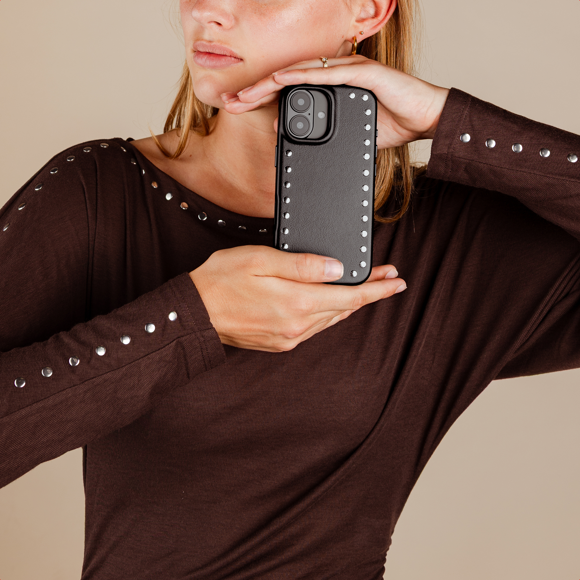 A woman holds a black phone case with studs. She is wearing a brown top.