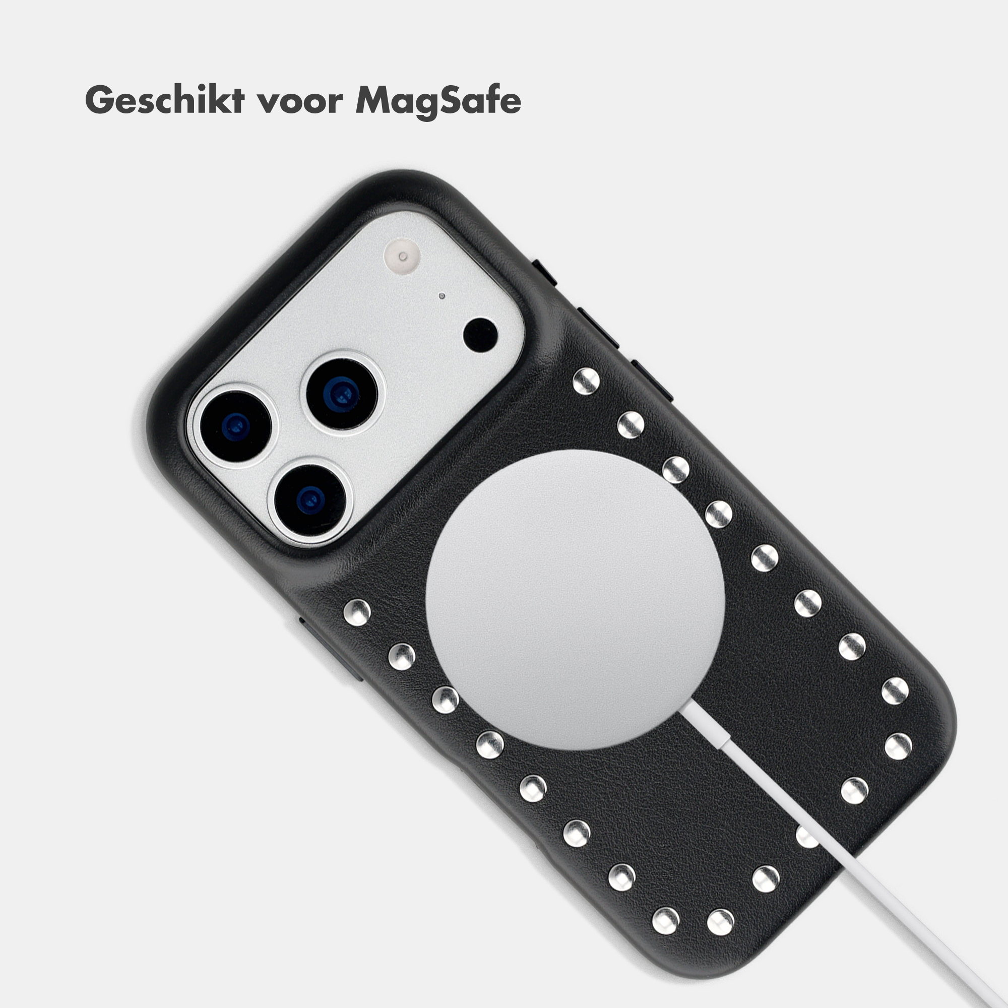 Schwarzes Handy mit Nieten und MagSafe-Ladegerät, auf hellem Hintergrund.