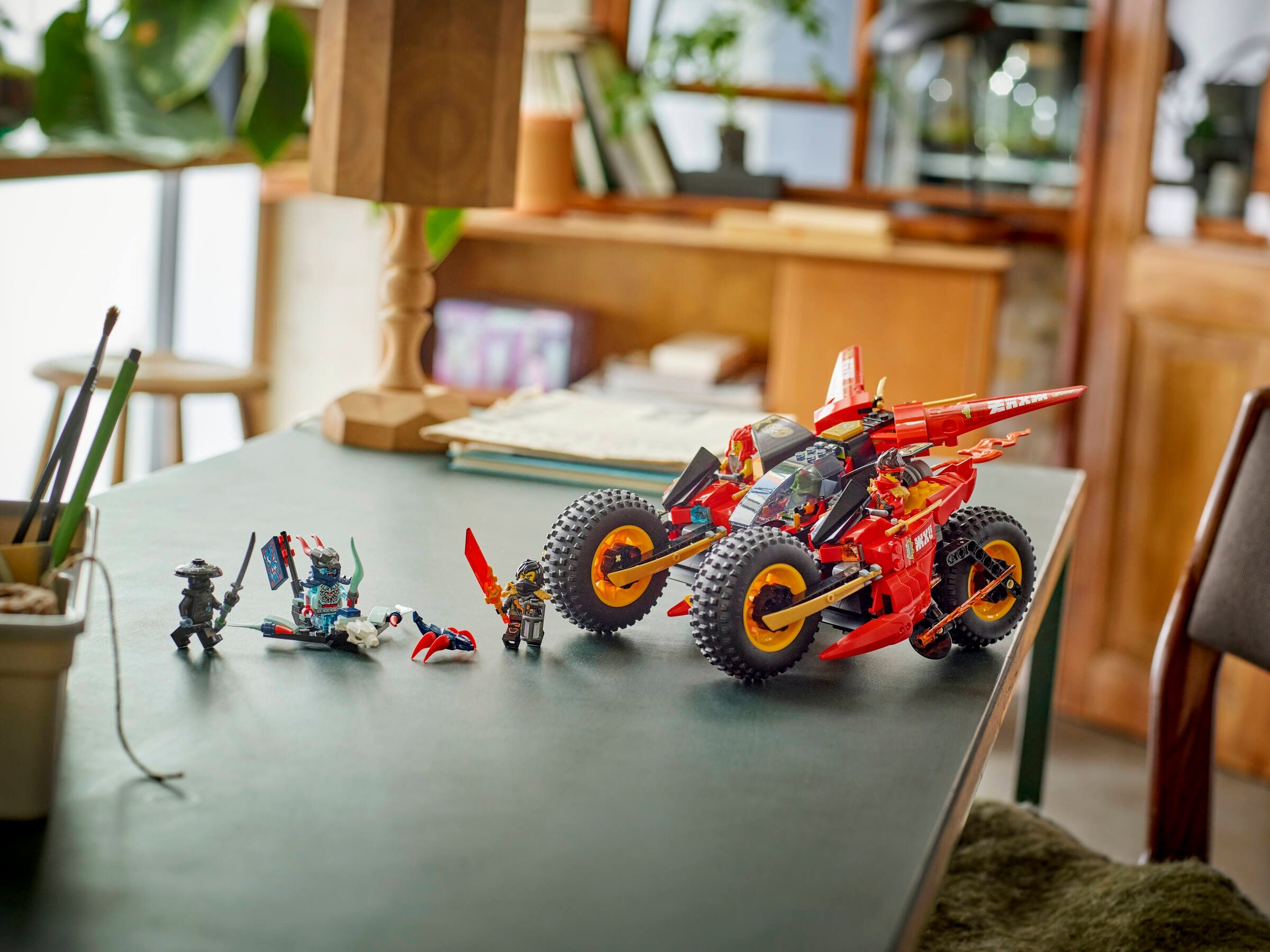 Lego Ninjago Figuren und ein roter Rennwagen mit großen Rädern auf einem dunklen Tisch.