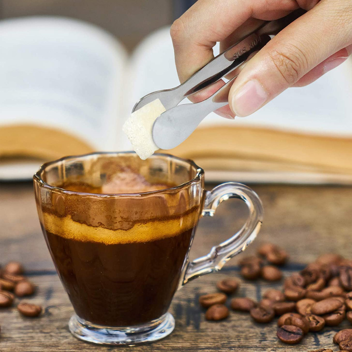 Eine Hand hält eine Zange, die einen Zuckerwürfel über einer Espressotasse hält.