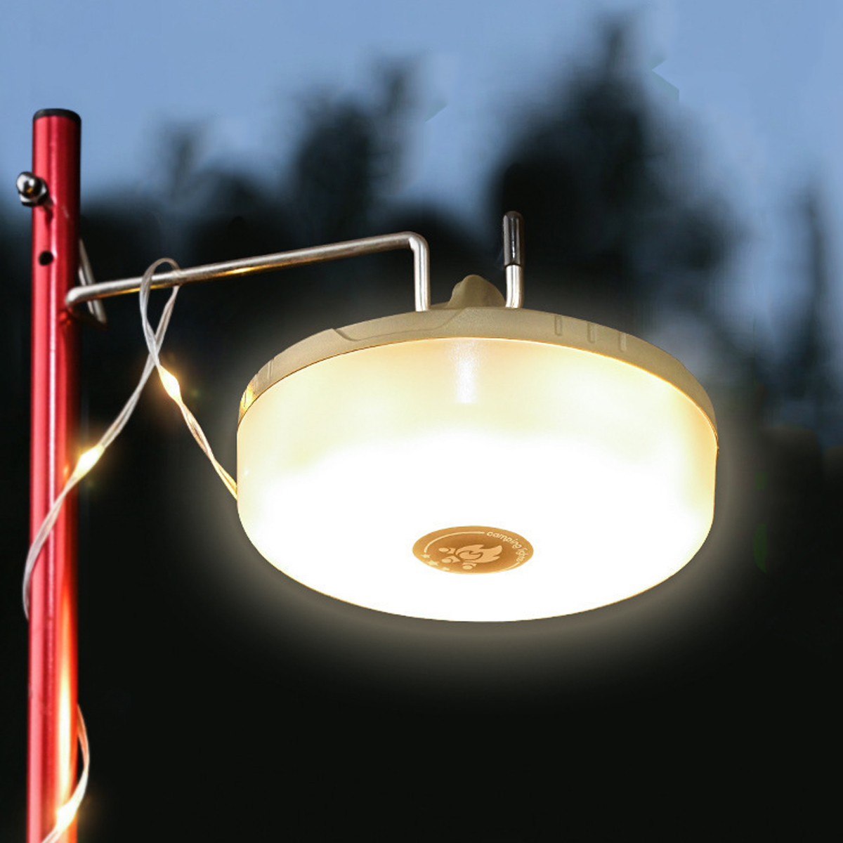Eine helle Campinglaterne hängt an einem roten Stab, mit Lichterketten drumherum.