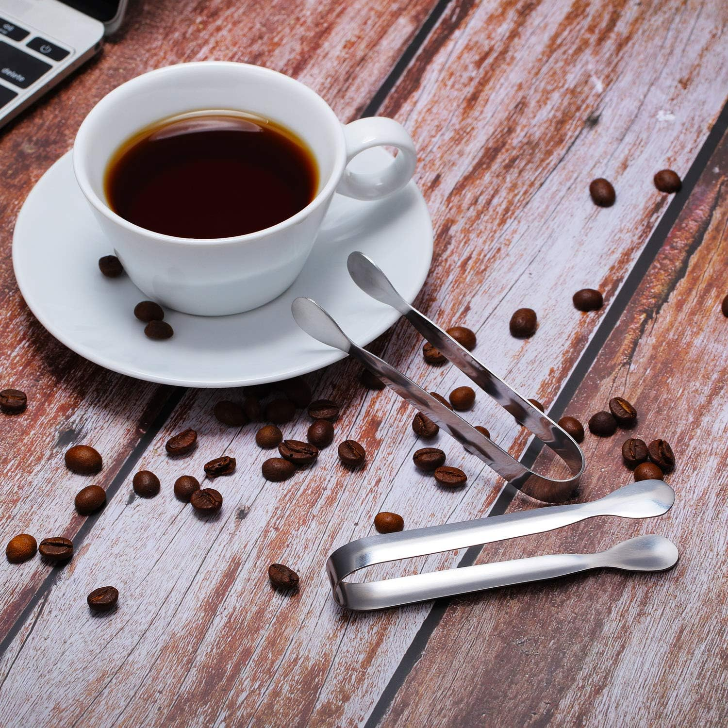 Tasse Kaffee mit Kaffeebohnen und Zange auf Holztisch