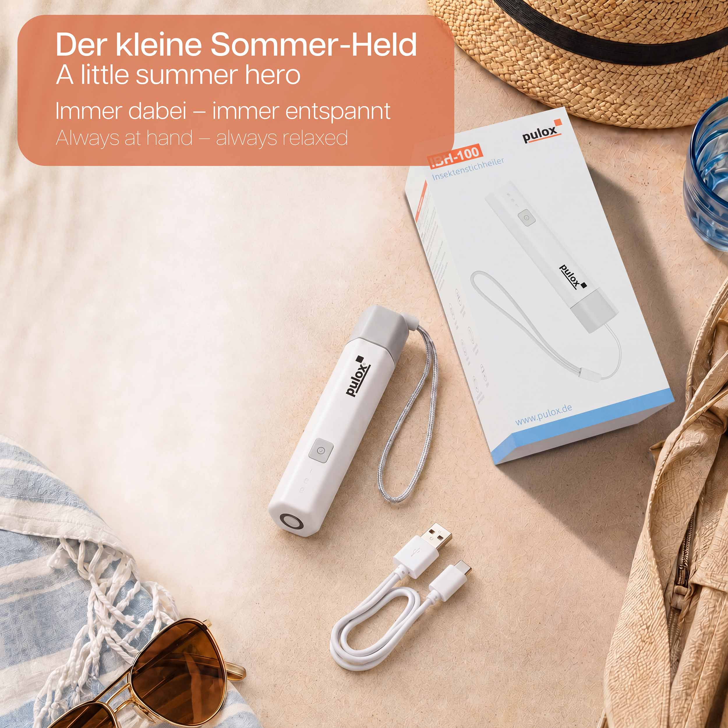 Ein weißer Insektenstichheiler mit USB-Kabel, Sonnenbrille und Hut auf Sand.