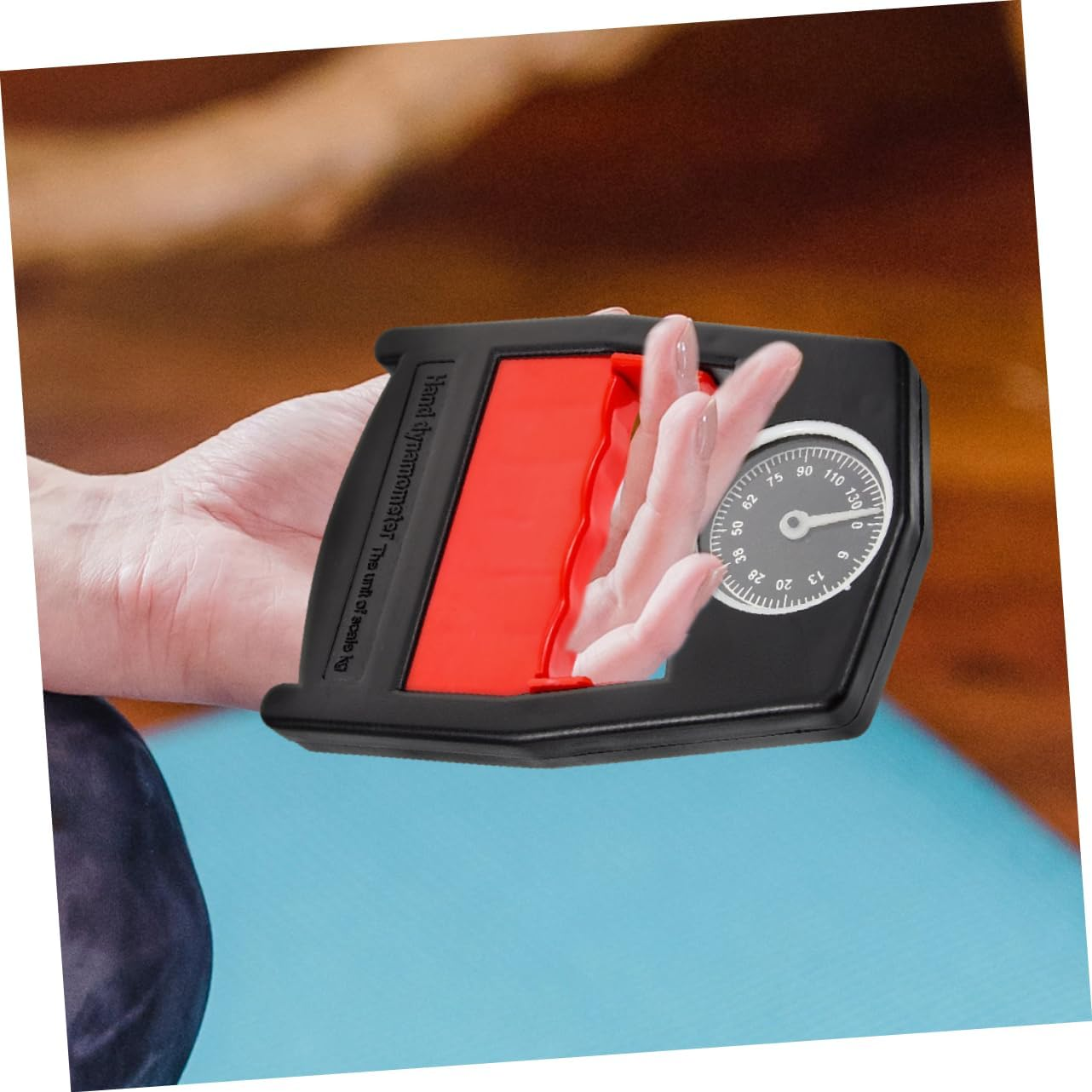 Eine Hand drückt einen schwarzen Dynamometer mit rotem Griff und Wähle.
