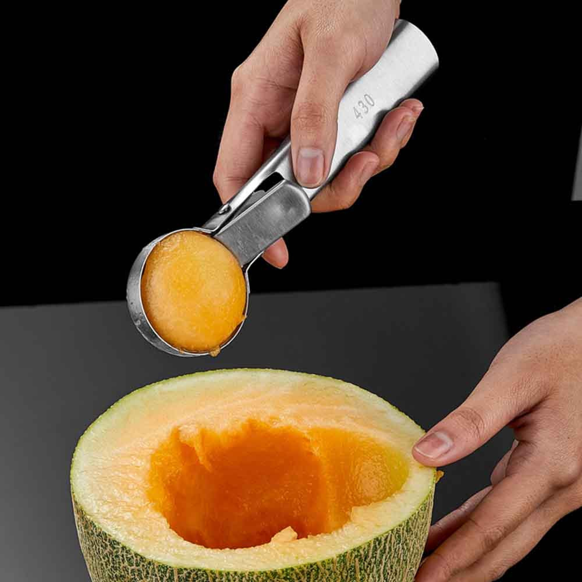 Eine Hand benutzt einen Löffel, um eine Kugel aus einer halbierten Honigmelone zu formen.