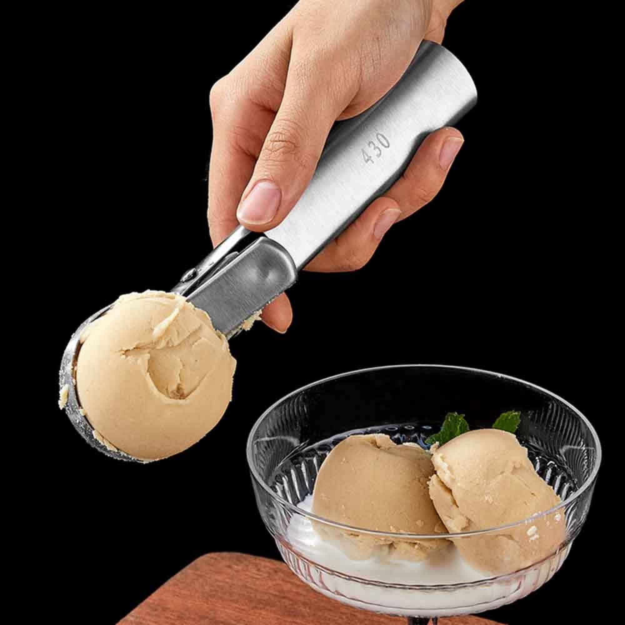 Eine Hand hält einen Eisportionierer mit einer Kugel hellbraunem Eis über einer Glasschale.