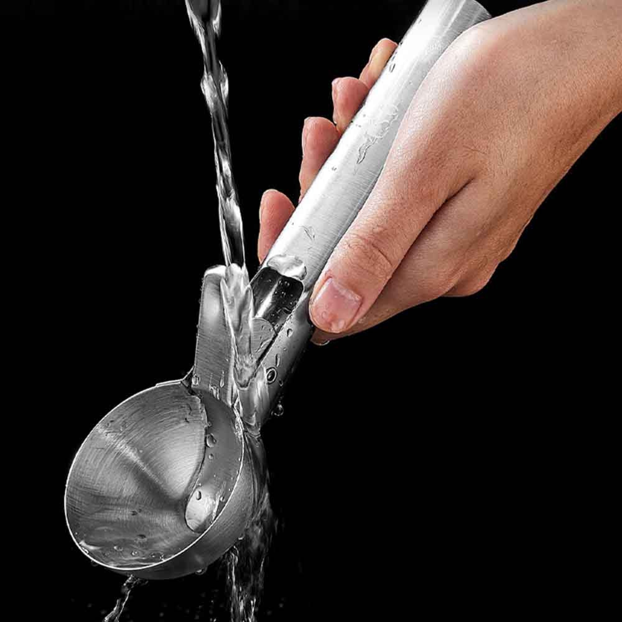 Eine Hand hält einen silbernen Eisportionierer, während Wasser darüber läuft.