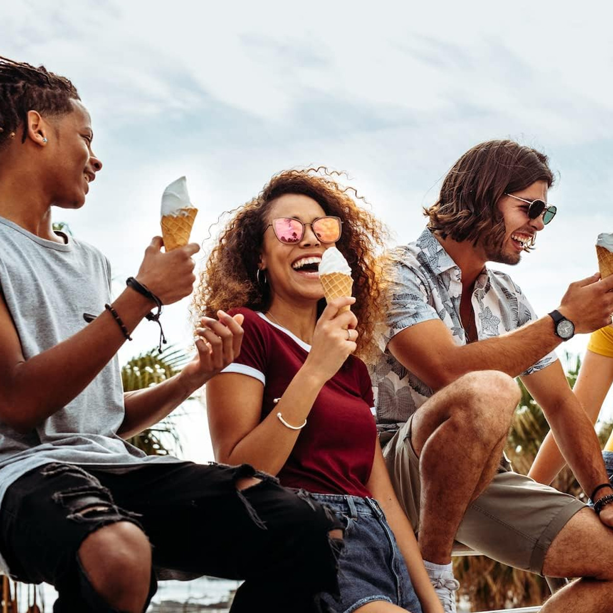 Drei junge Leute sitzen draußen und essen Eiscreme. Sie lachen und sehen glücklich aus.