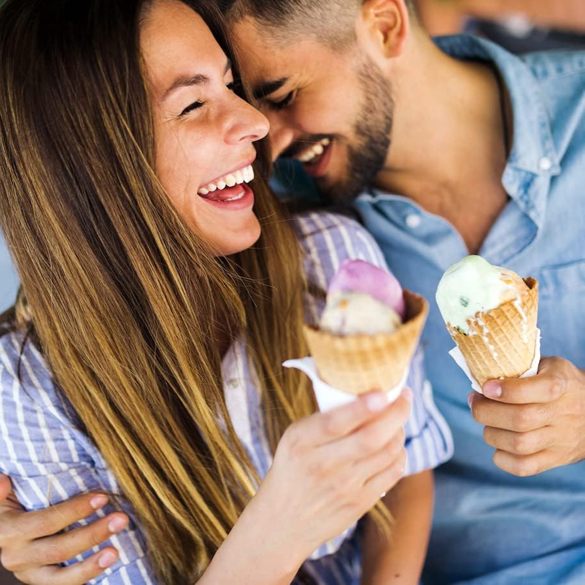 Ein Paar lacht und hält Eis in Waffeln. Der Mann umarmt die Frau.