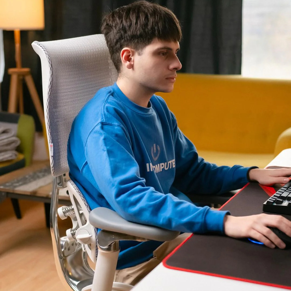 Ein Mann in einem blauen Pullover sitzt auf einem Bürostuhl und spielt am Computer.