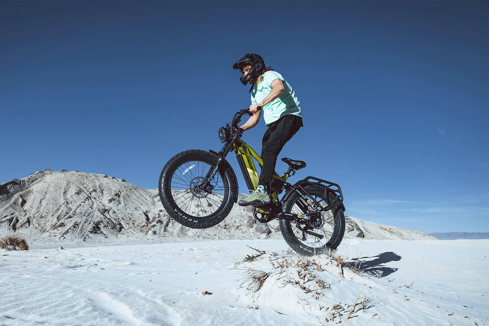 Ein Mann springt mit einem E-Bike über eine Schneelandschaft, im Hintergrund Berge.