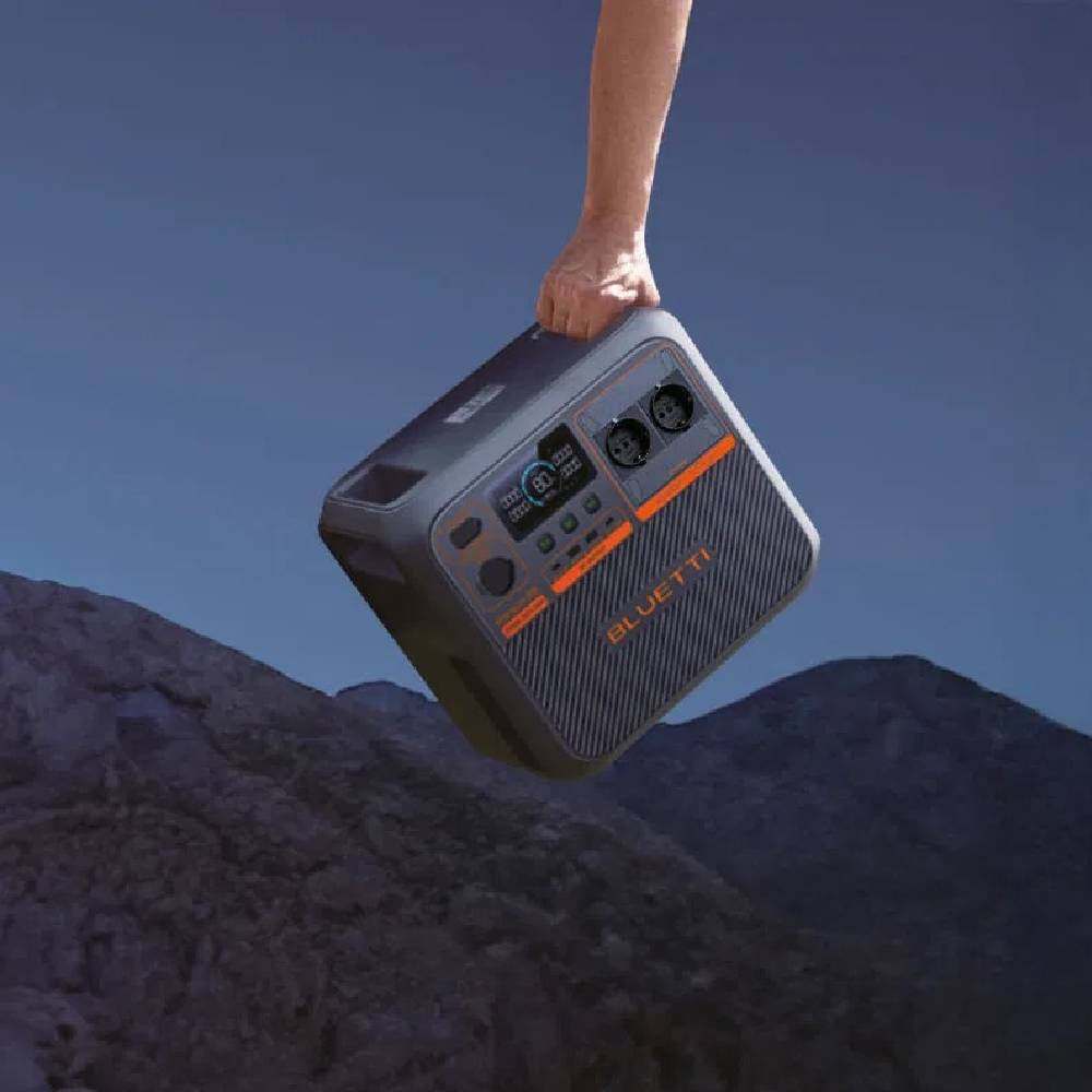 Una mano tiene una centrale elettrica portatile contro un paesaggio montano al tramonto.
