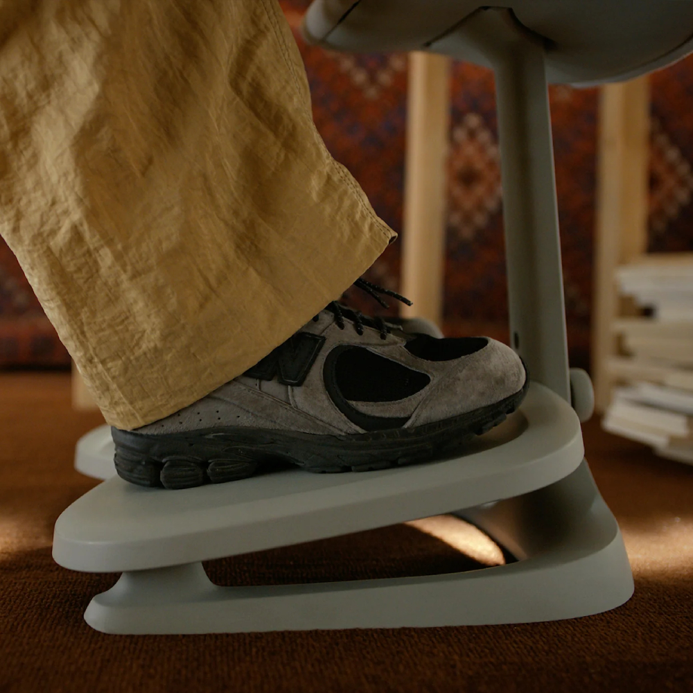 Un piede con scarpa da ginnastica grigia e pantaloni kaki poggia su un attrezzo ginnico grigio.