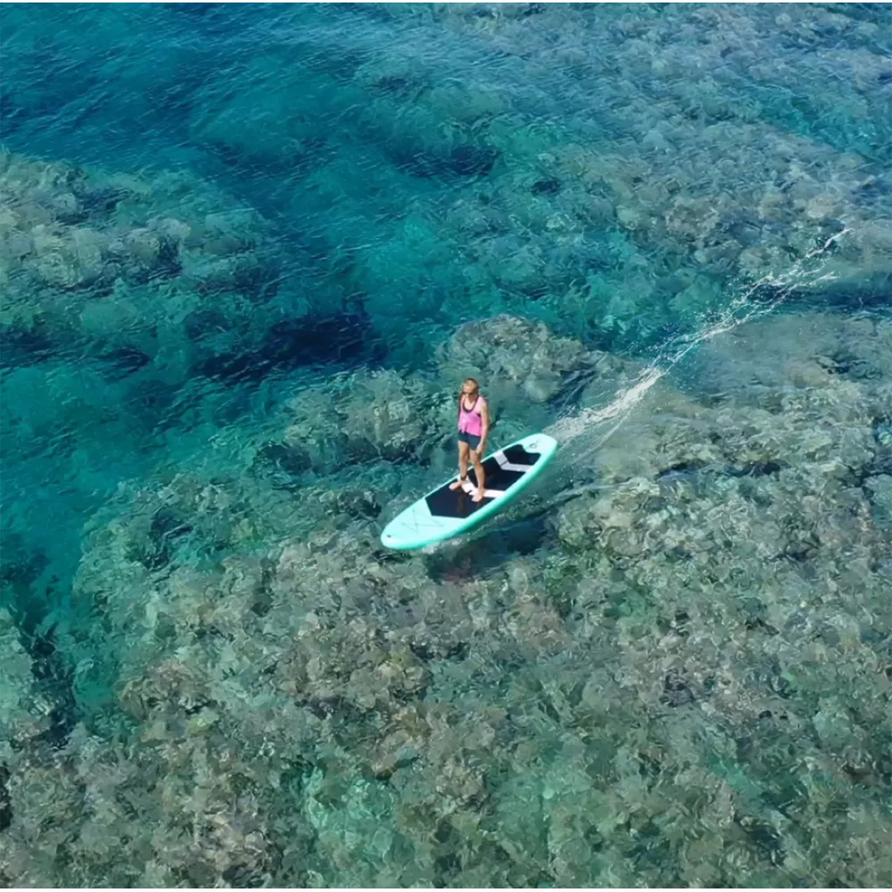 Mercan resiflerinin üzerindeki turkuaz suda paddleboard üzerinde bir kadın.