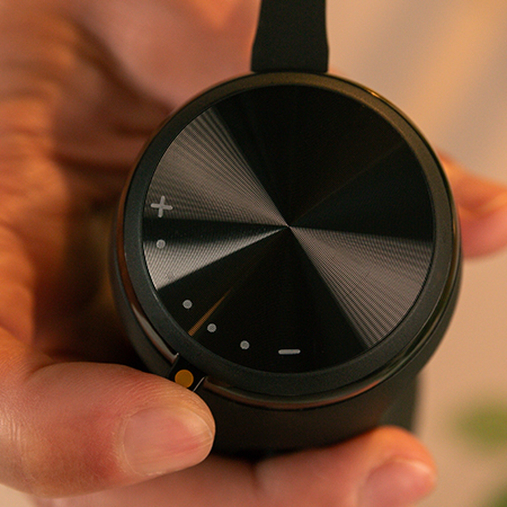 Una mano tiene un auricolare nero con quadrante argentato e spie luminose.