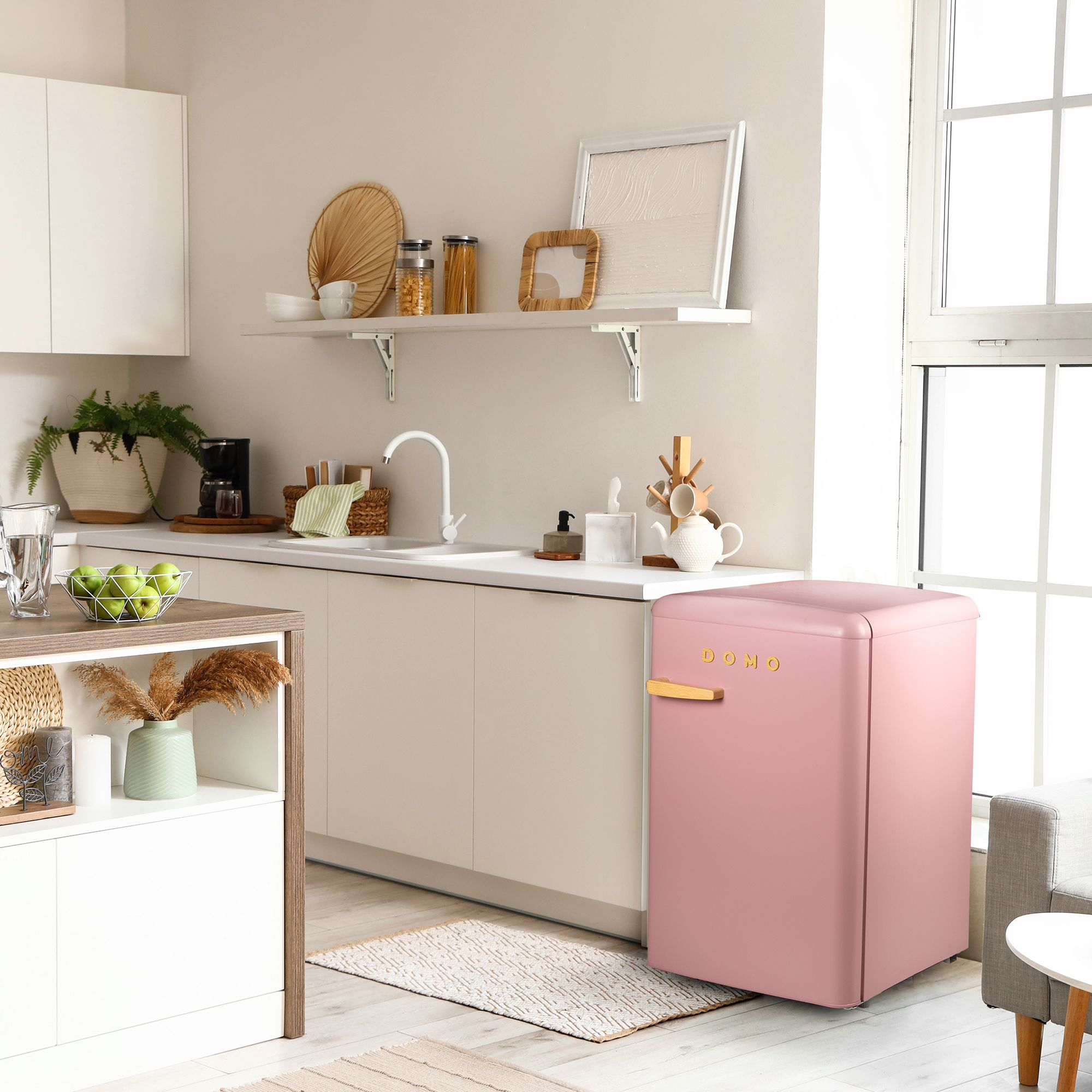 Une cuisine rétro rose avec un réfrigérateur, un évier, une cafetière et une coupe de pommes.