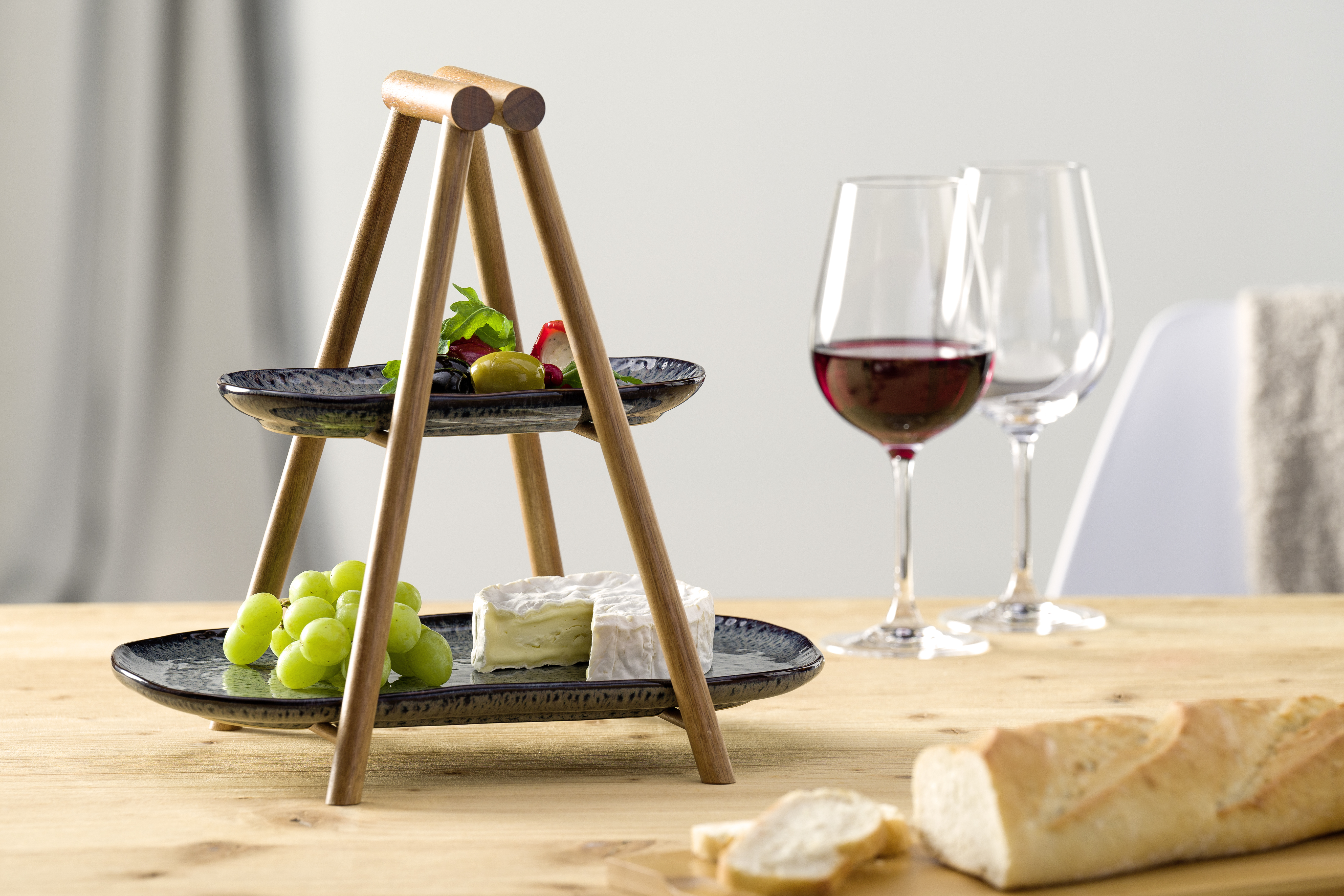 Zweistufige Servierplatte mit Käse, Trauben, Oliven und Brot, daneben Weingläser.