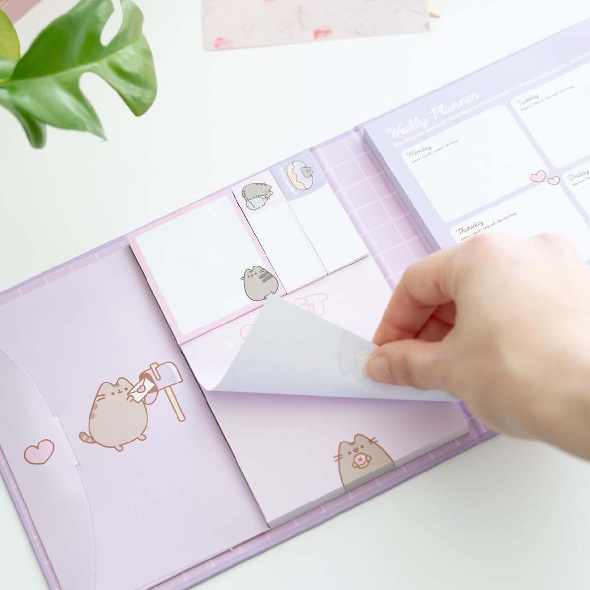 Eine Hand zieht einen Haftnotizblock aus einem lila Planer mit Pusheen-Katzenmotiven.