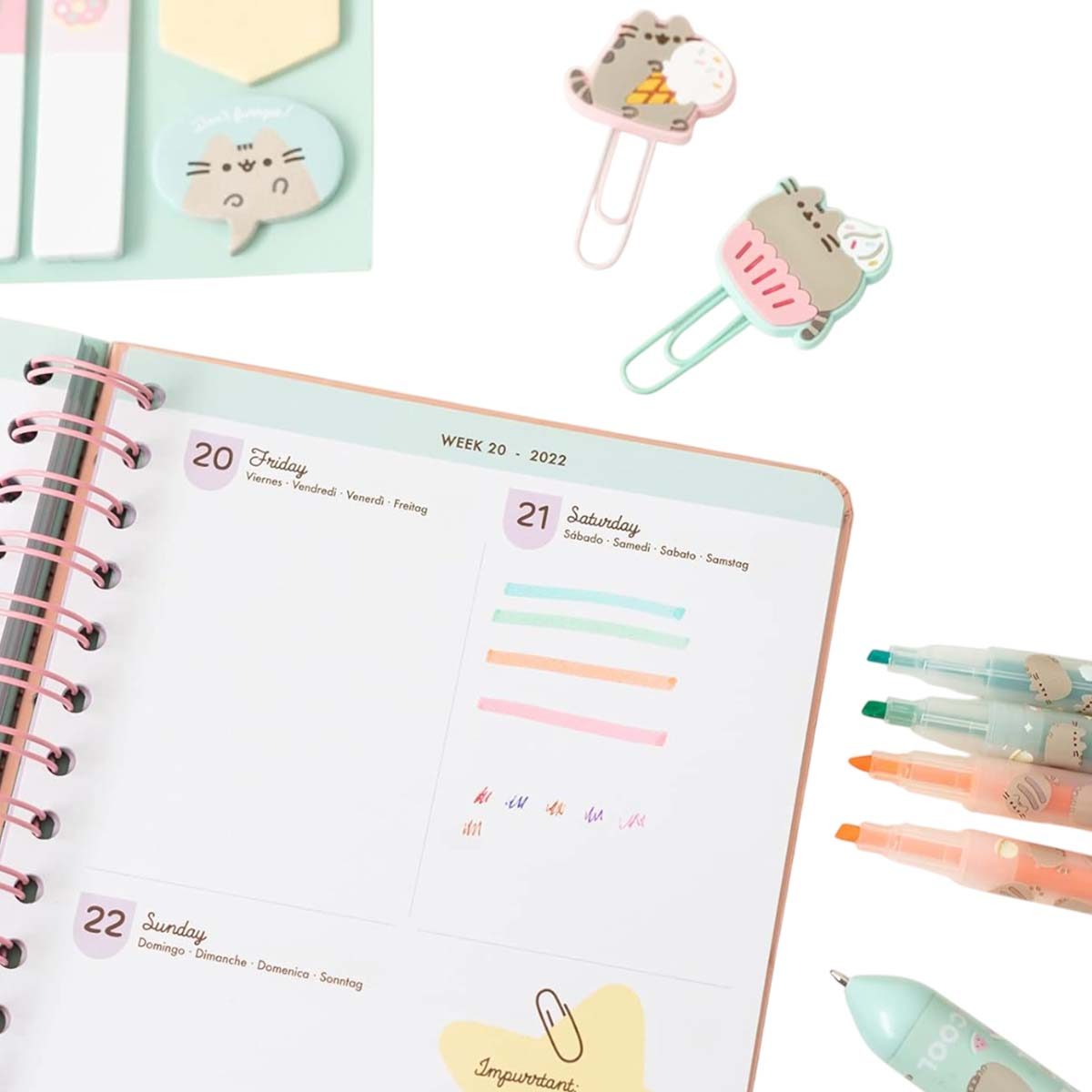 Ein geöffnetes Notizbuch mit Pusheen-Clips und Stiften daneben.