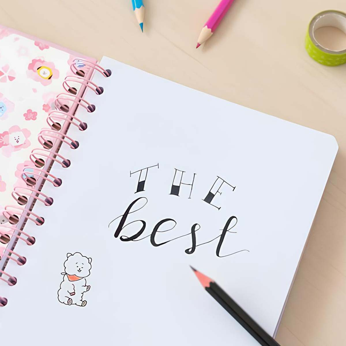 Ein Notizbuch mit der Aufschrift „The best“, Stifte und Klebeband auf einem Holztisch.