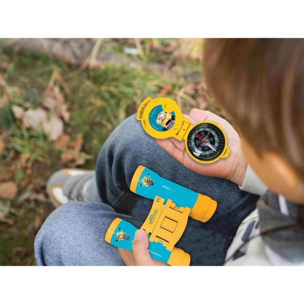 Un bambino tiene in mano un binocolo giallo a tema Minions e una bussola.