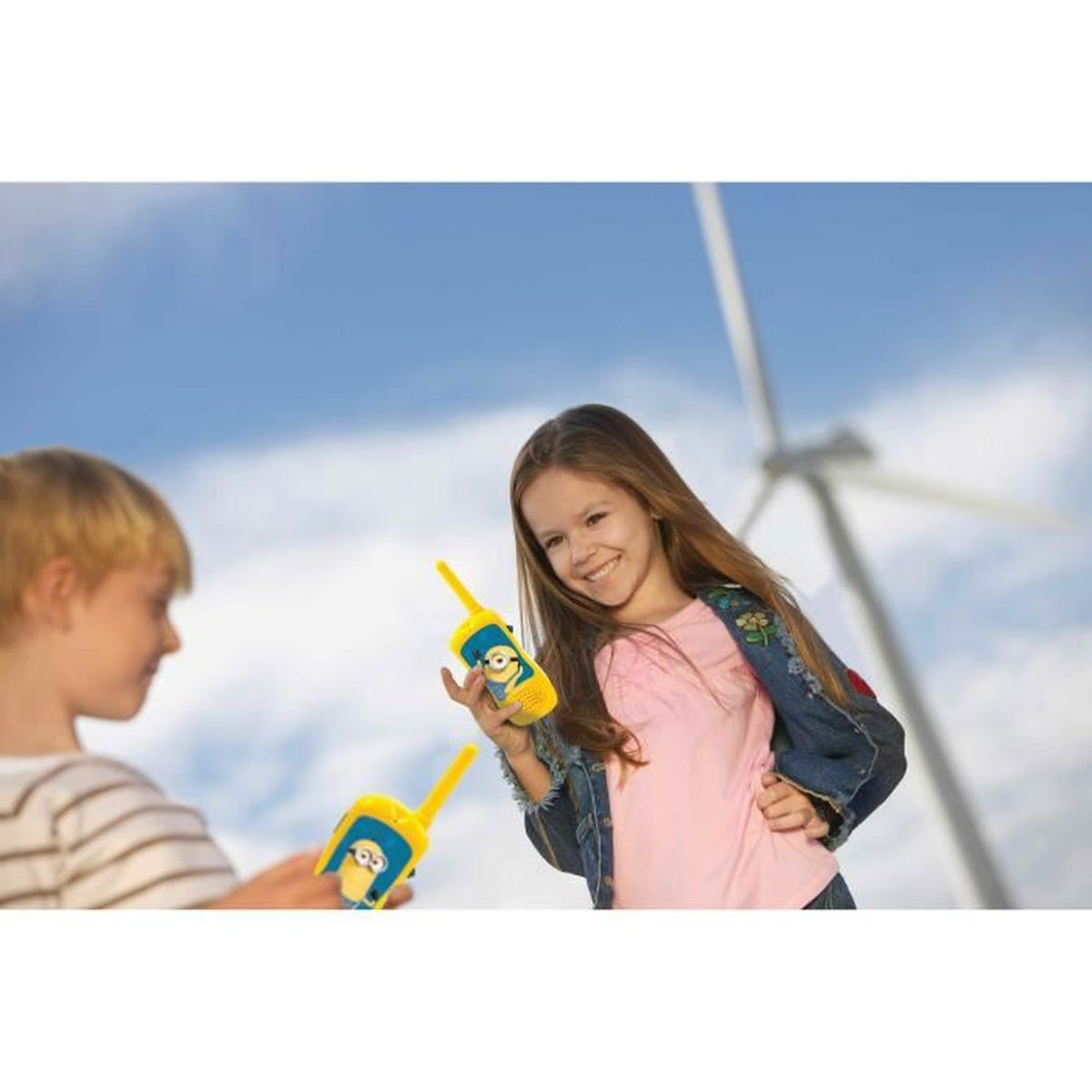 Due bambini tengono walkie-talkie gialli con Minions davanti a una turbina eolica.
