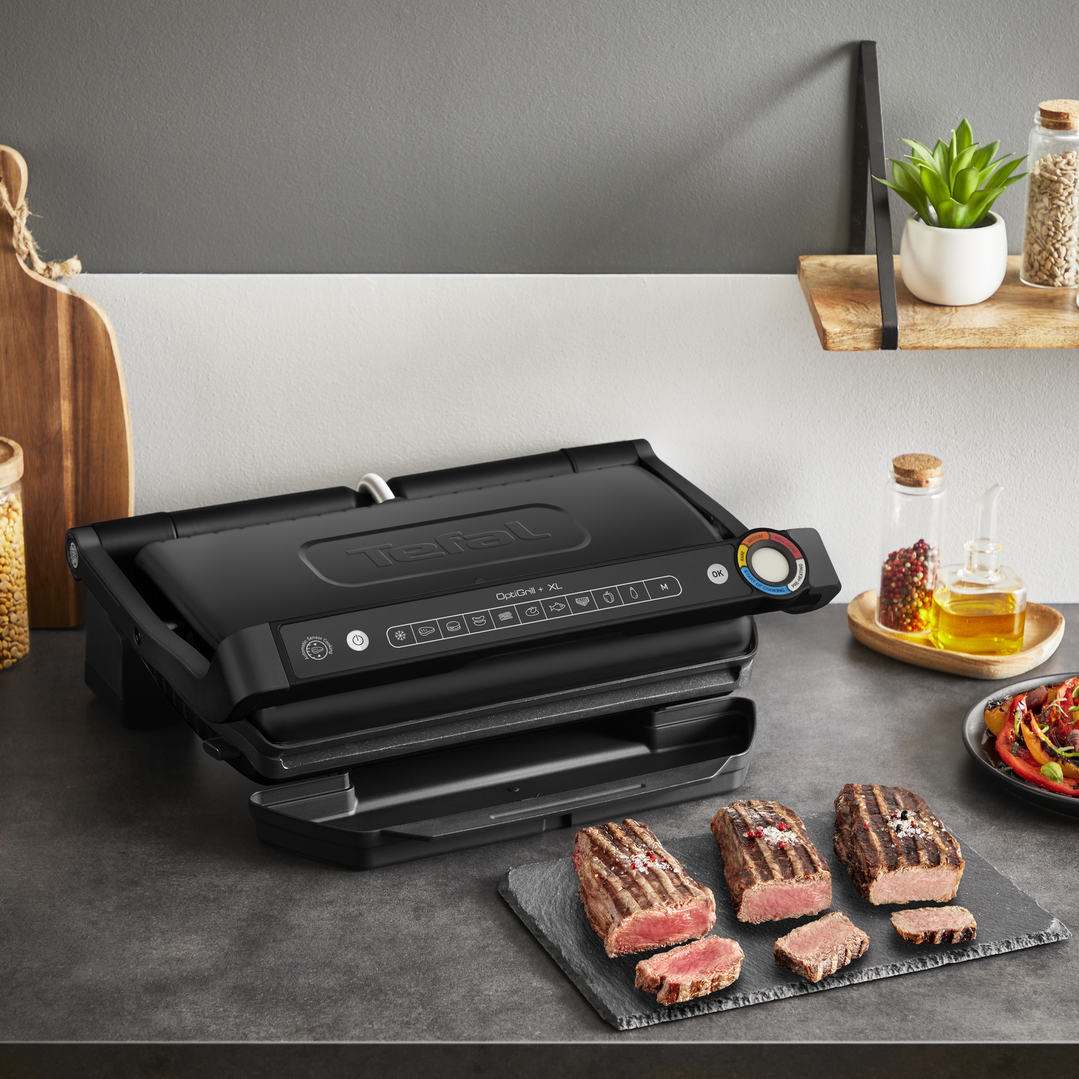 Ein schwarzer Kontaktgrill mit gebratenen Steaks und Gemüse auf einem Tisch.