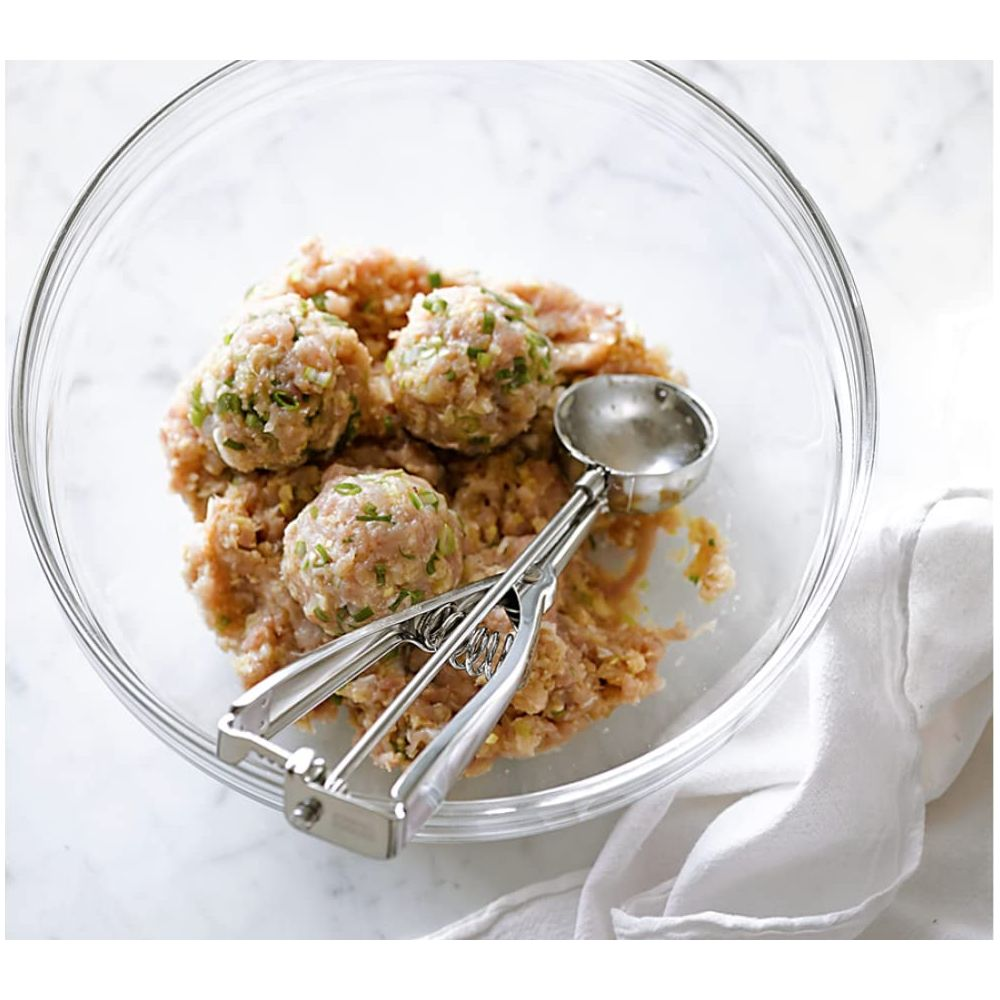 Una ciotola di vetro con carne macinata e polpette, e uno scavino per polpette.