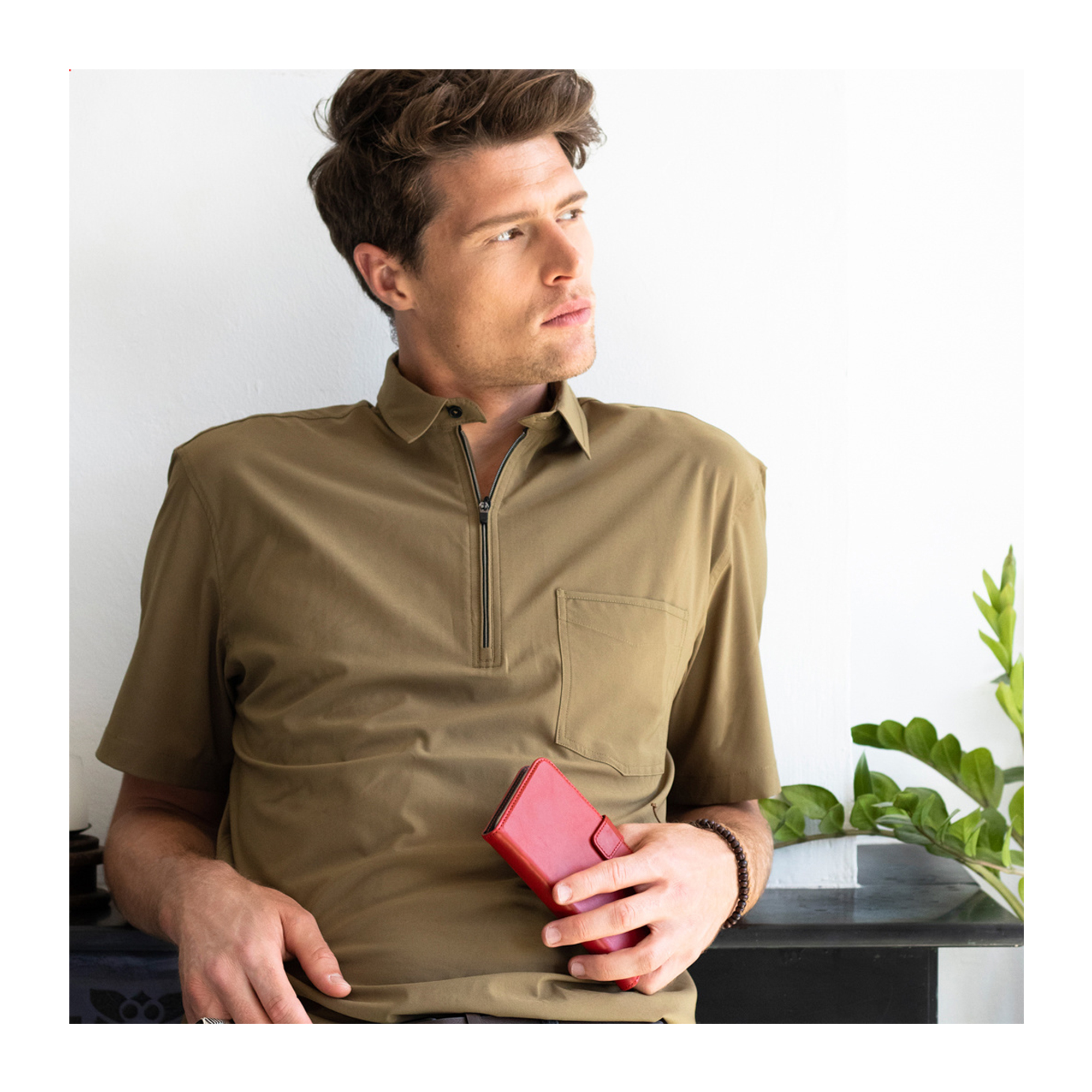 Un uomo con camicia kaki tiene un portafoglio rosso.