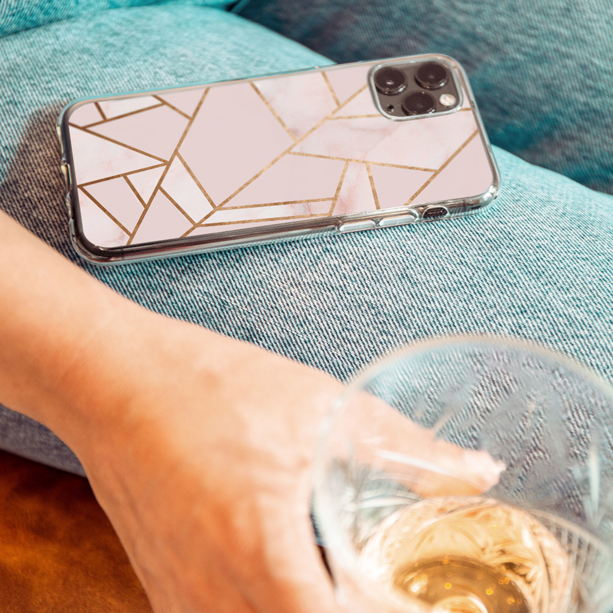 Un telefono rosa con motivo marmorizzato e linee dorate appoggiato sui jeans.