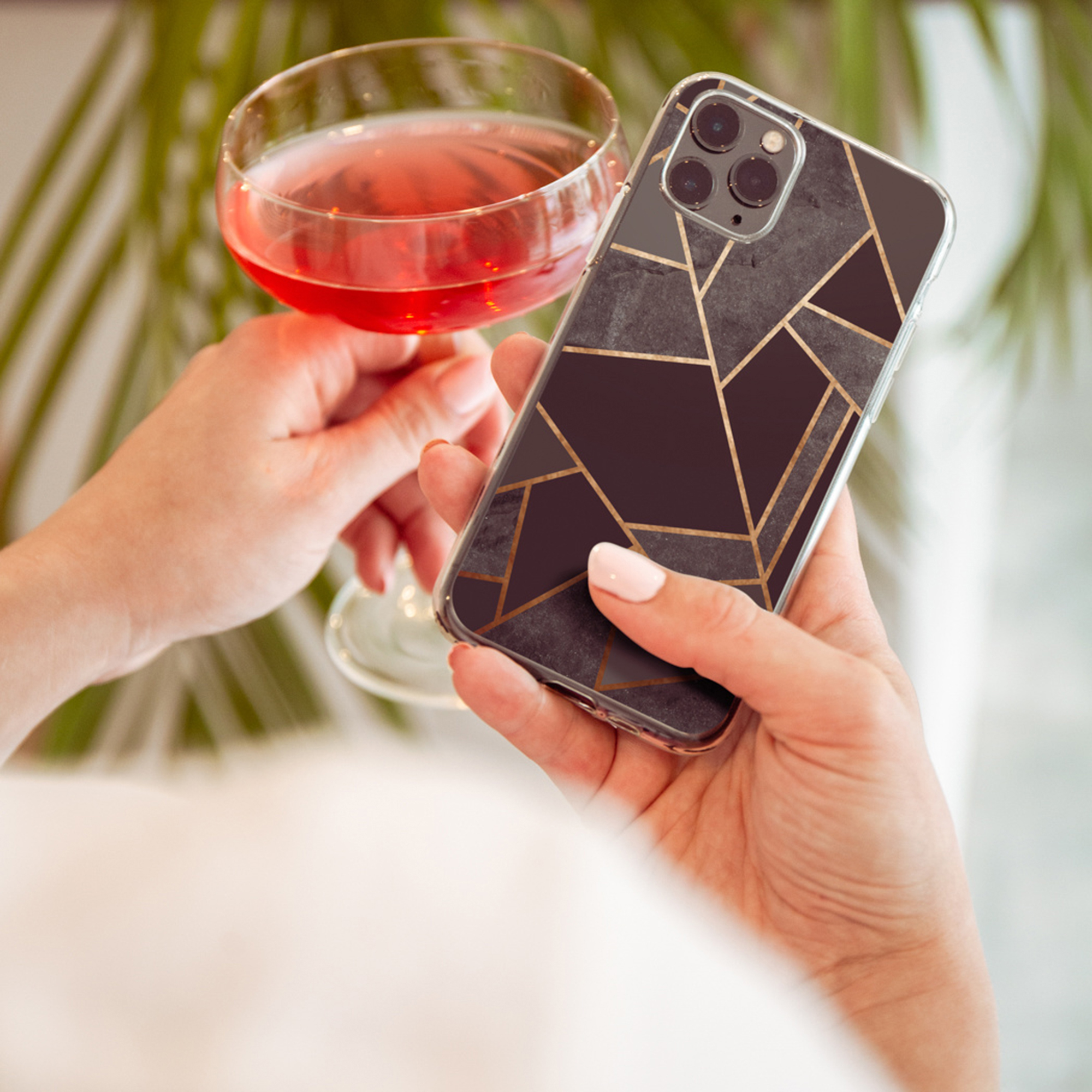 Mani tengono un telefono con cover in marmo e un bicchiere di bevanda rosa.