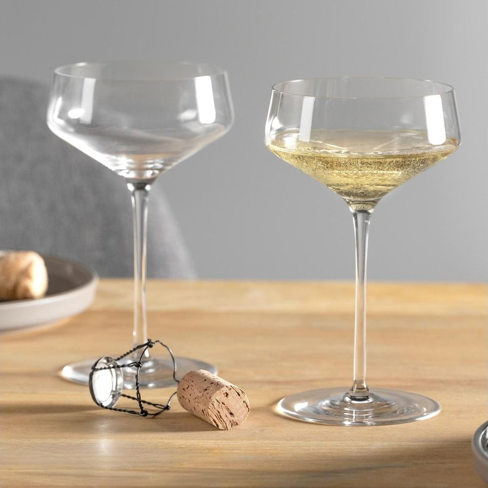 Zwei Weingläser auf einem Holztisch, eines mit Champagner, daneben ein Korken.