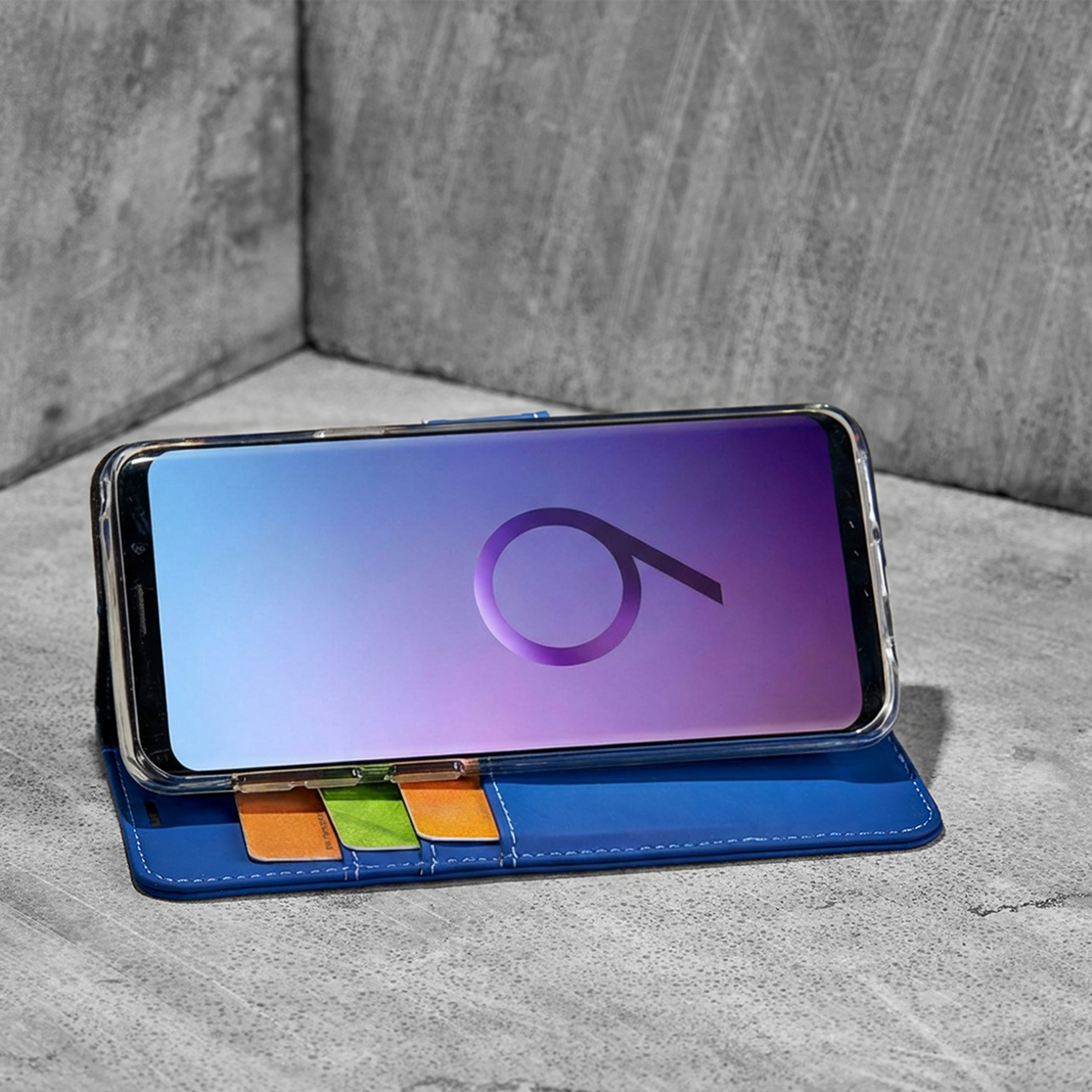 Uno smartphone in una custodia blu con slot per carte su cemento.
