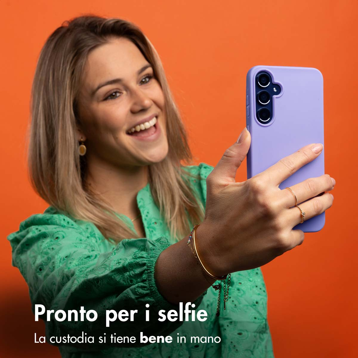 Een vrouw maakt een selfie met een paarse telefoon tegen een oranje achtergrond.