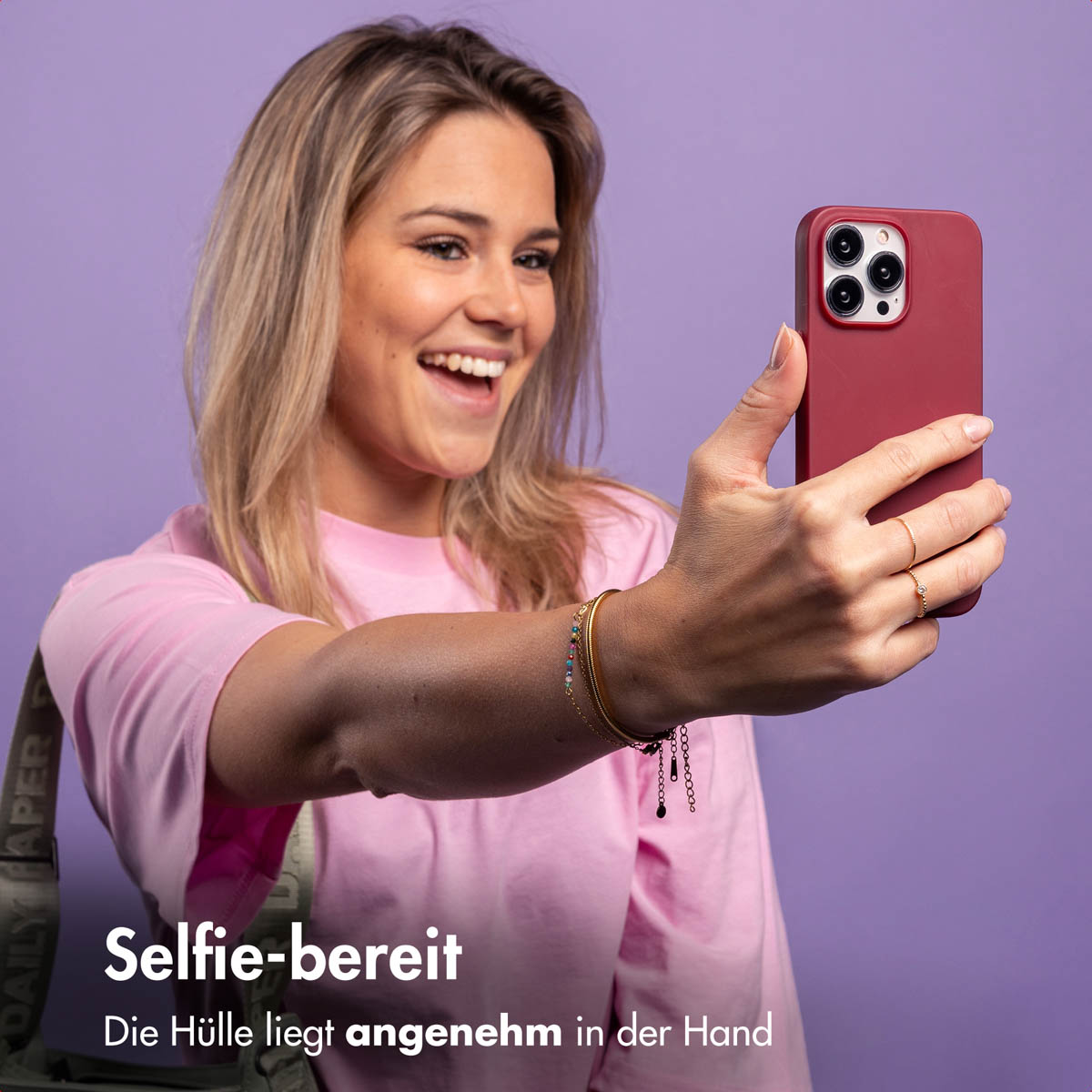 Una donna sorridente in camicia rosa si fa un selfie con cover rossa su sfondo viola.