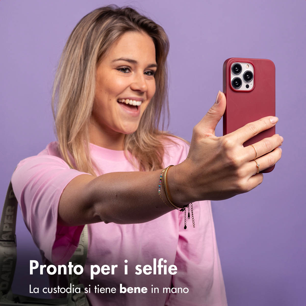 Una donna in maglietta rosa si fa un selfie con un telefono rosso su sfondo viola.