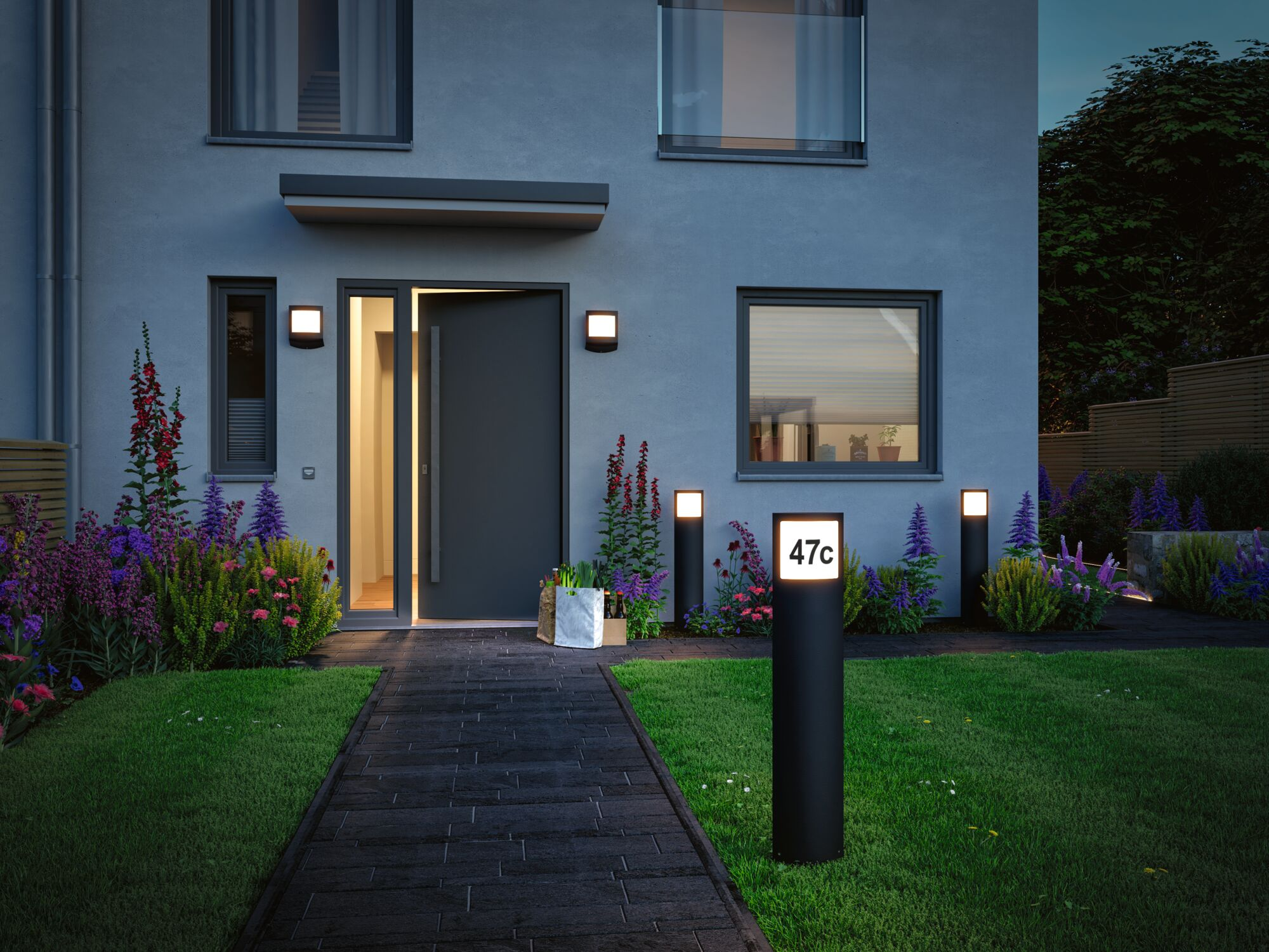 Ein modernes graues Haus mit offener Tür, beleuchtetem Weg und Blumen. Hausnummer 47c.