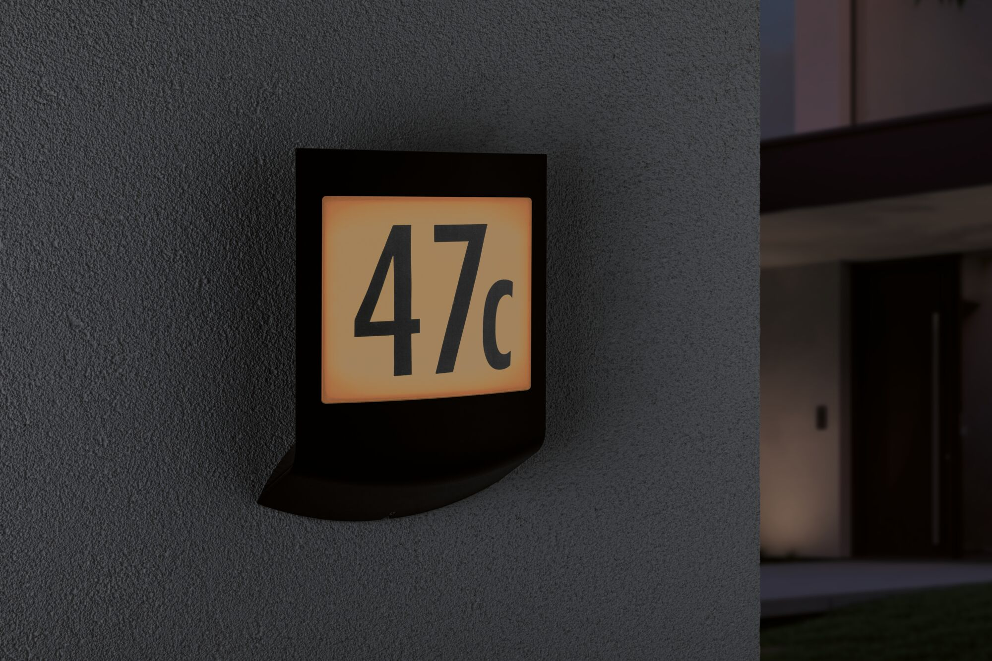 Ein beleuchtetes Hausnummernschild mit der Aufschrift 47c an einer grauen Wand.