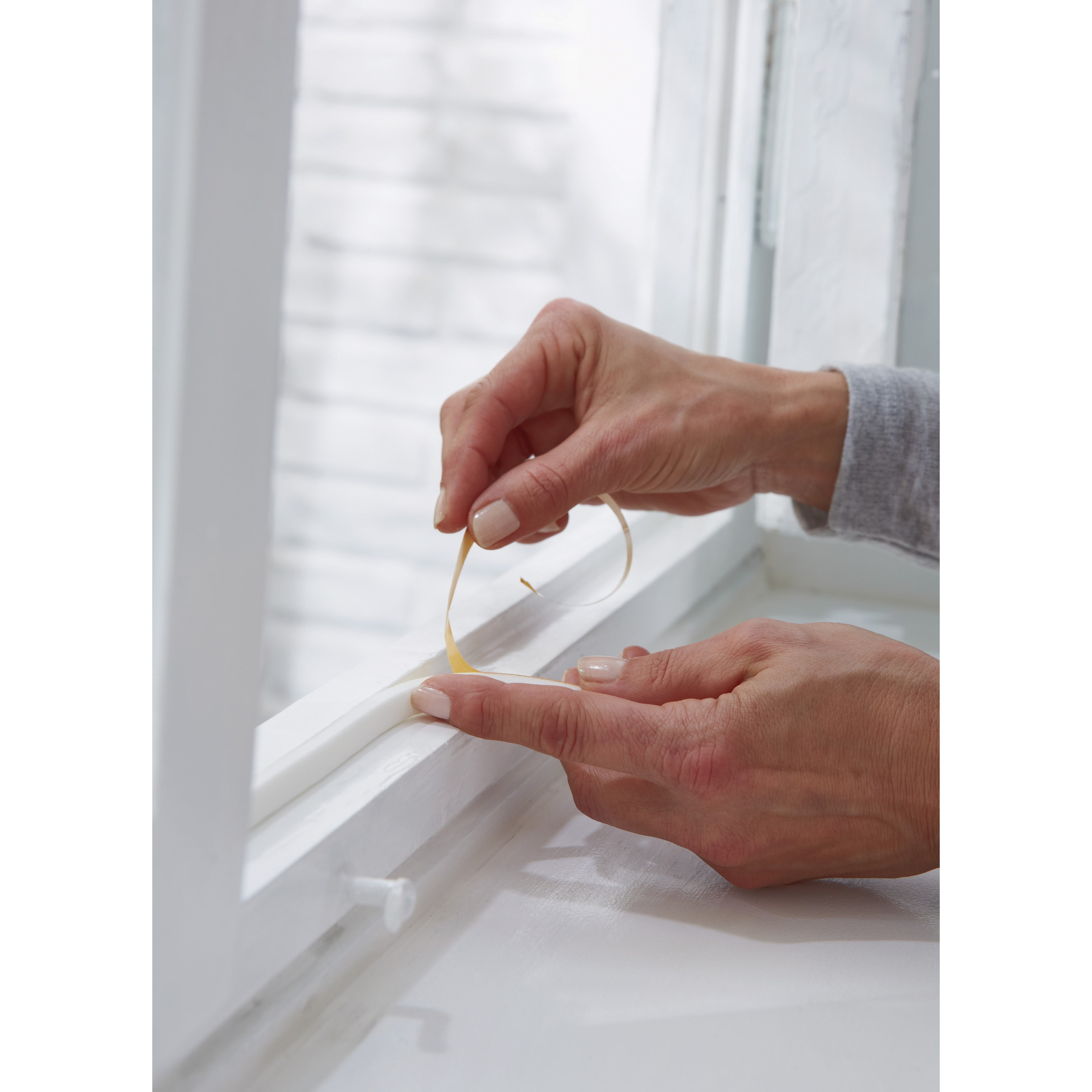 Hände bringen Klebeband an einem weißen Fensterrahmen an.