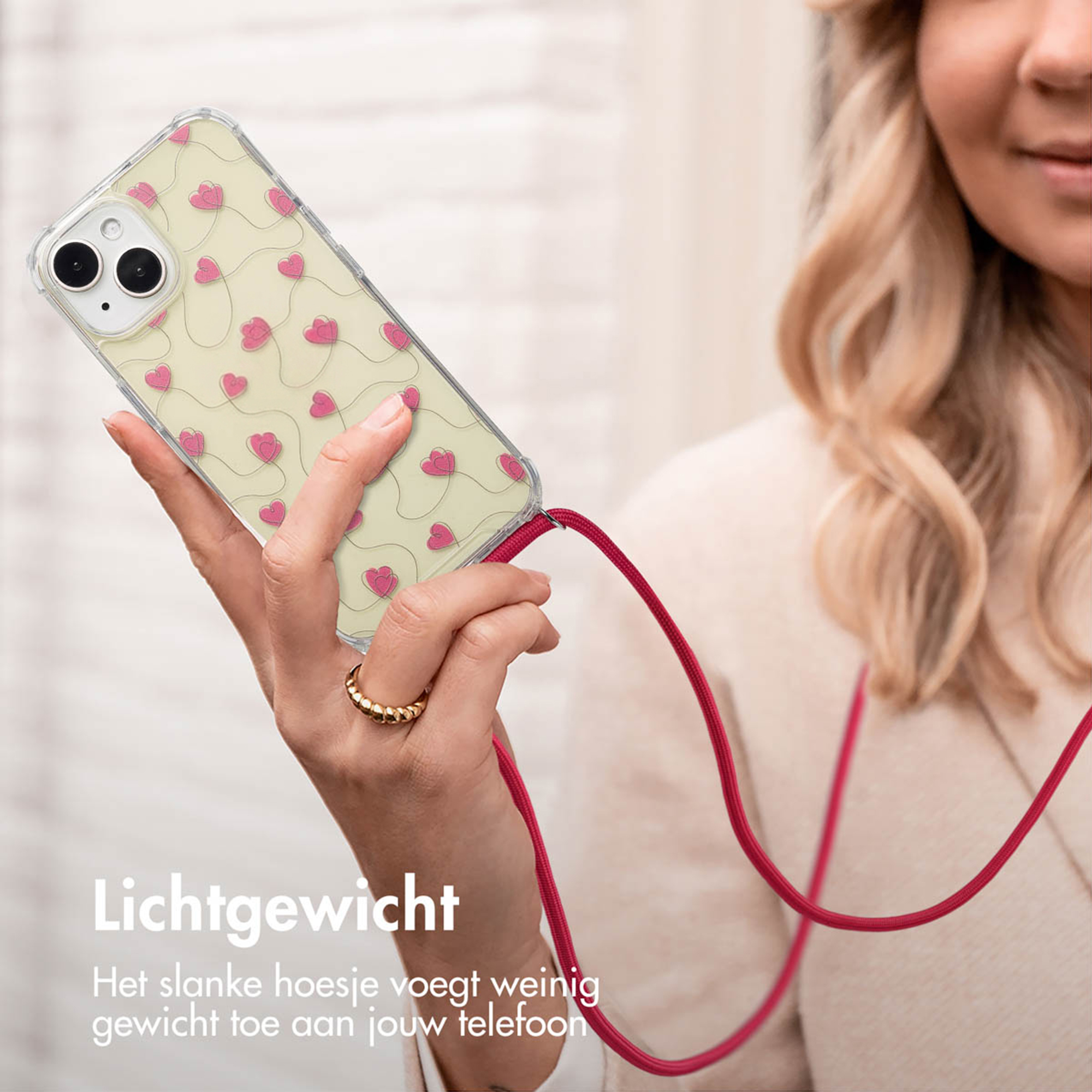 A hand holds a phone with pink hearts. A red cord is attached.