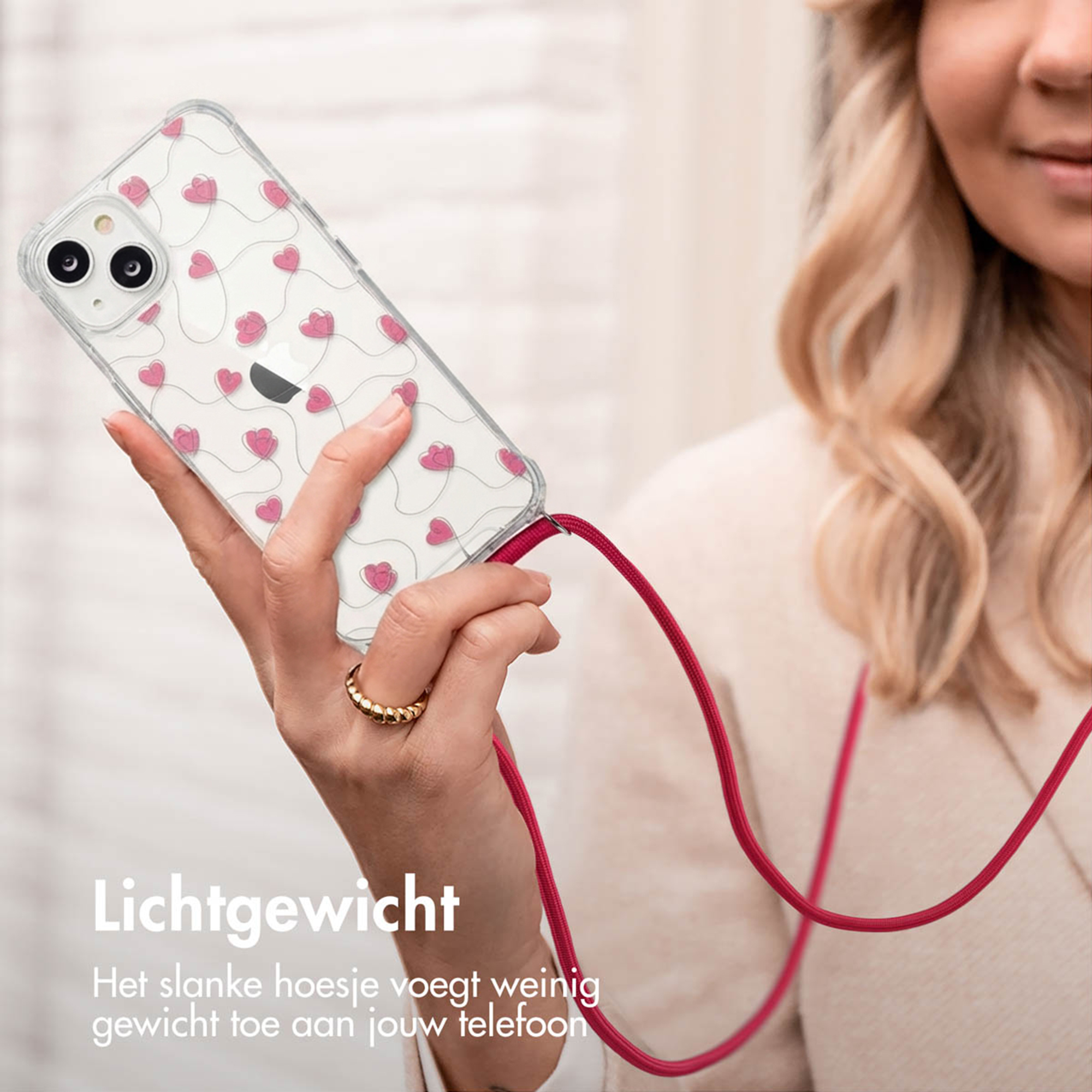Une main tient une coque de téléphone transparente avec des cœurs roses et un cordon rouge.